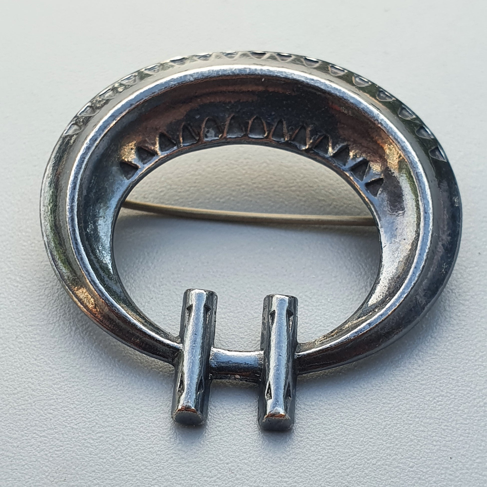 Silver penannular brooch with decorative edging and two protruding pins.