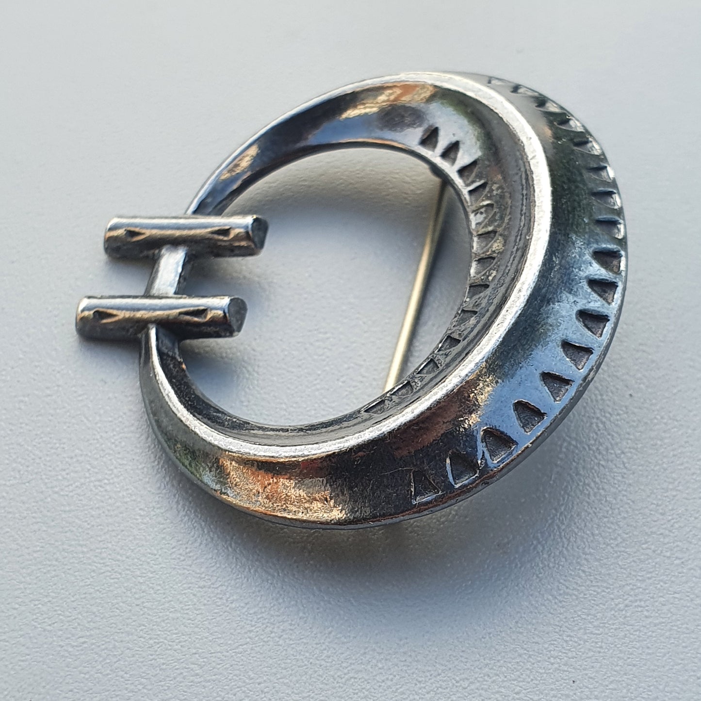 Oval-shaped metal belt buckle with decorative notches along its edge and a double-pronged clasp.