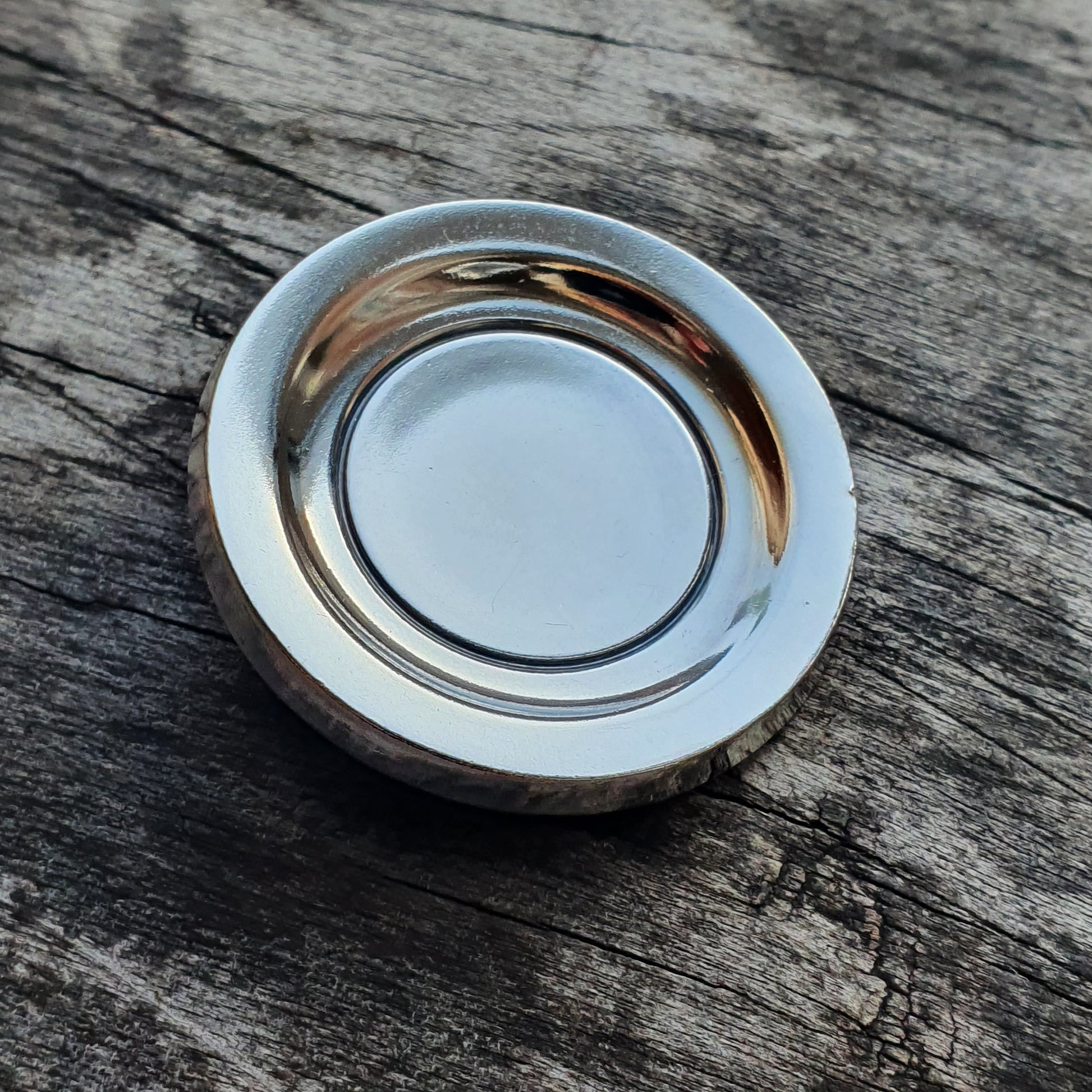 Shiny metal plate or dish with a circular indentation on a weathered wooden surface.