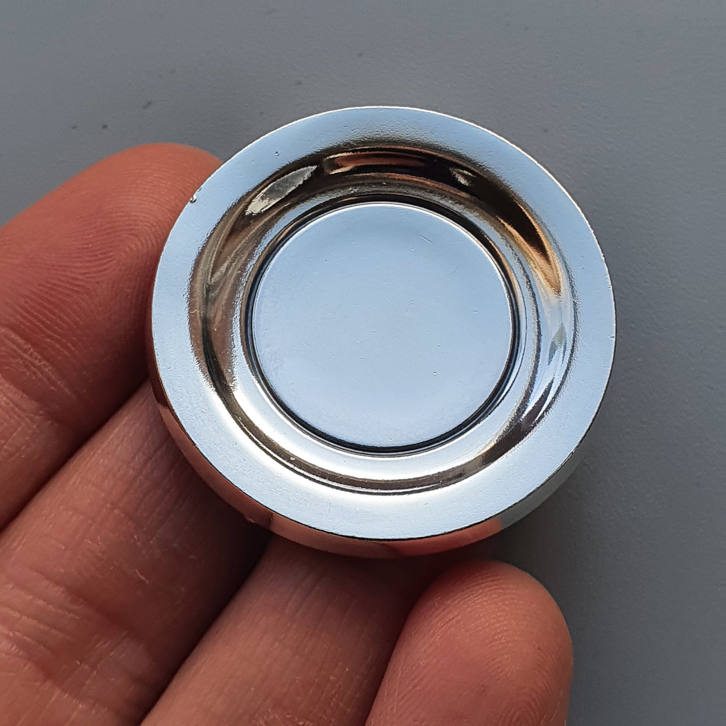 Circular metal button or knob with a reflective surface held between fingers.