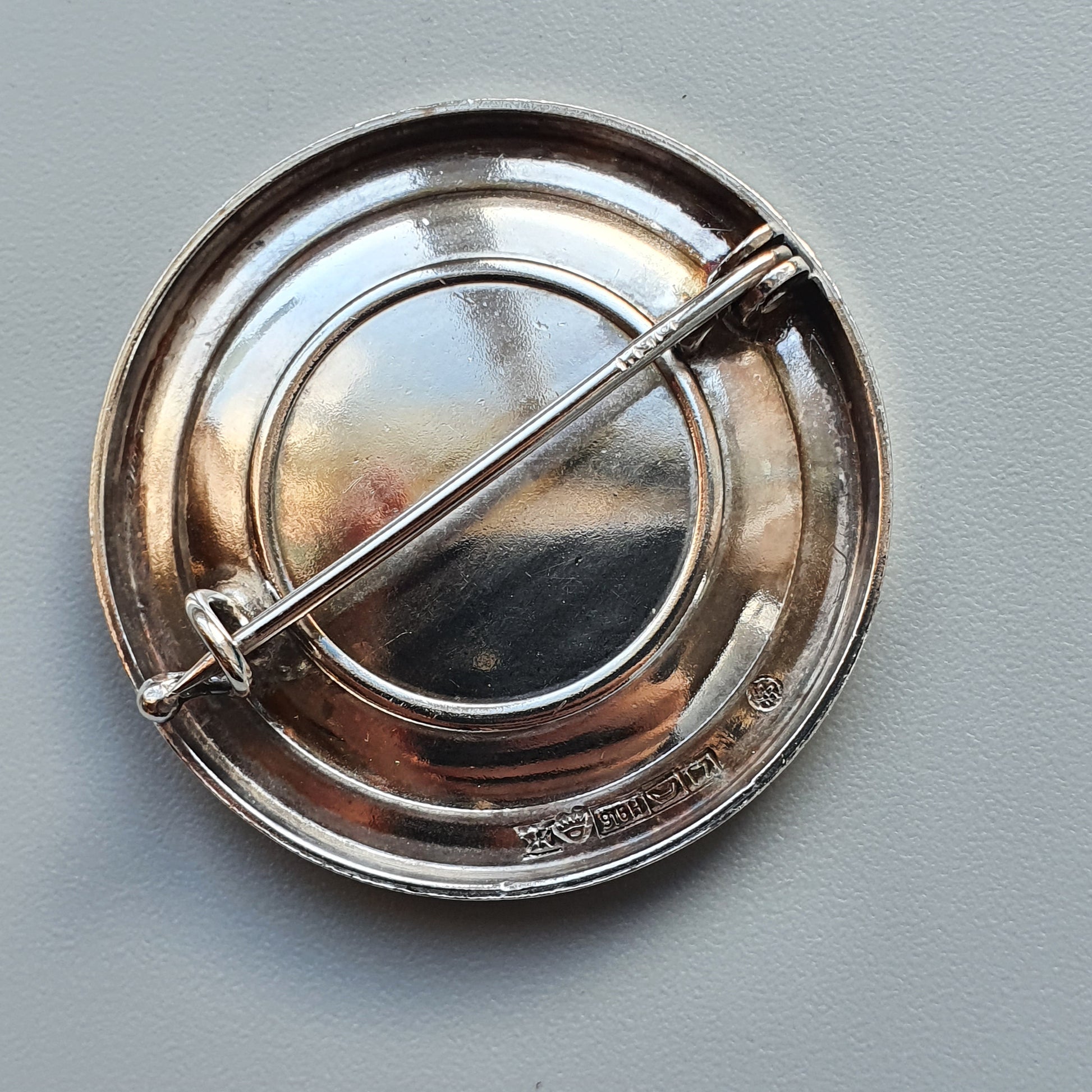 Circular silver brooch or pin with a central bar across its diameter.