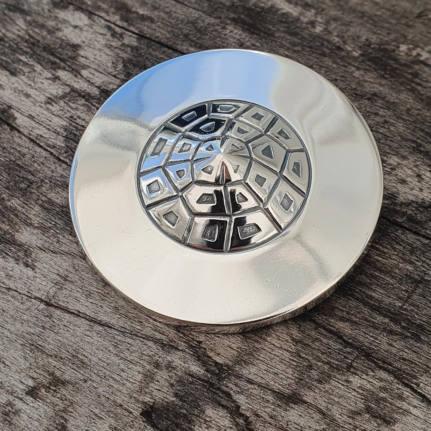 Metallic disc with a geometric pattern of raised shapes on its surface.