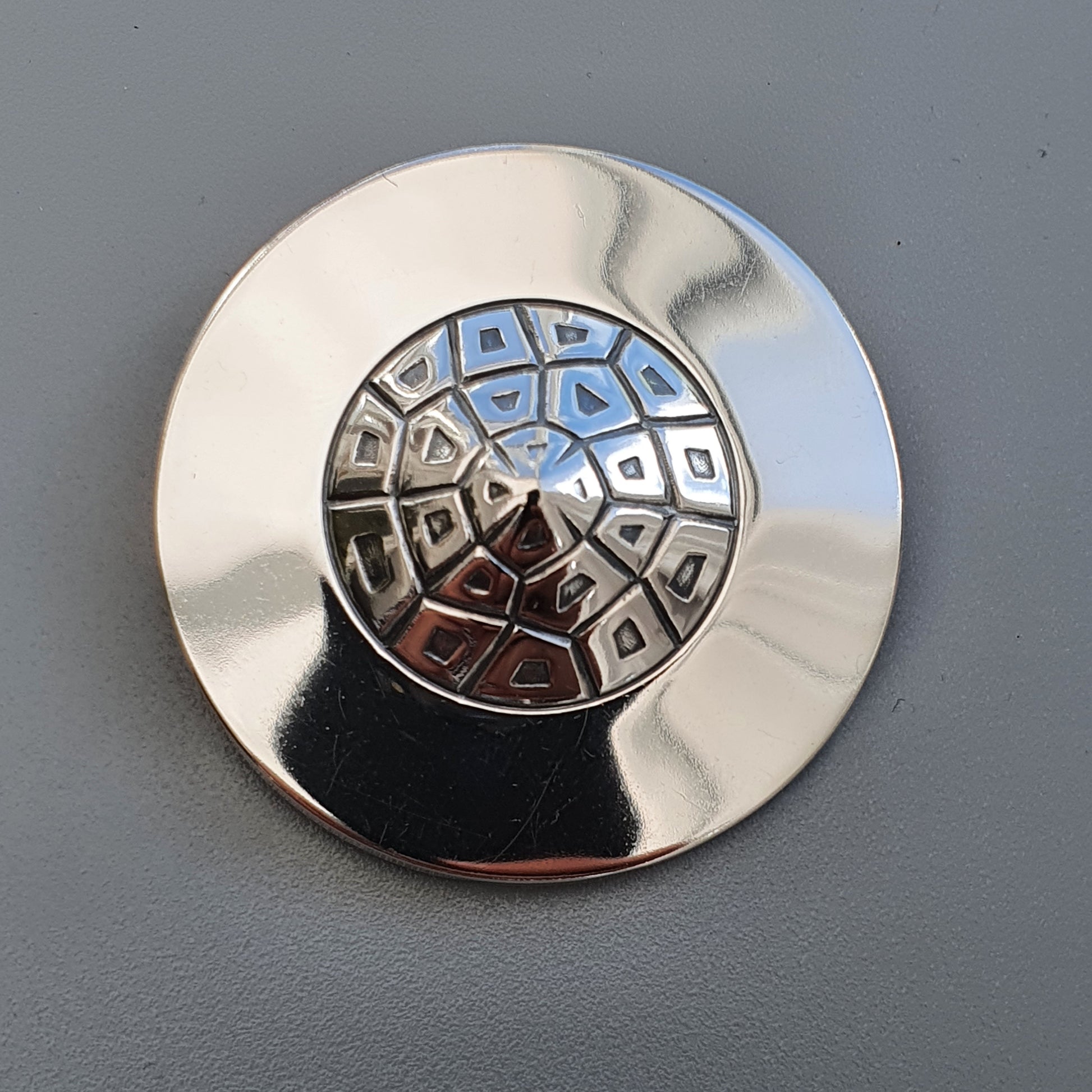 Shiny metallic button or knob with a geometric pattern on its face.