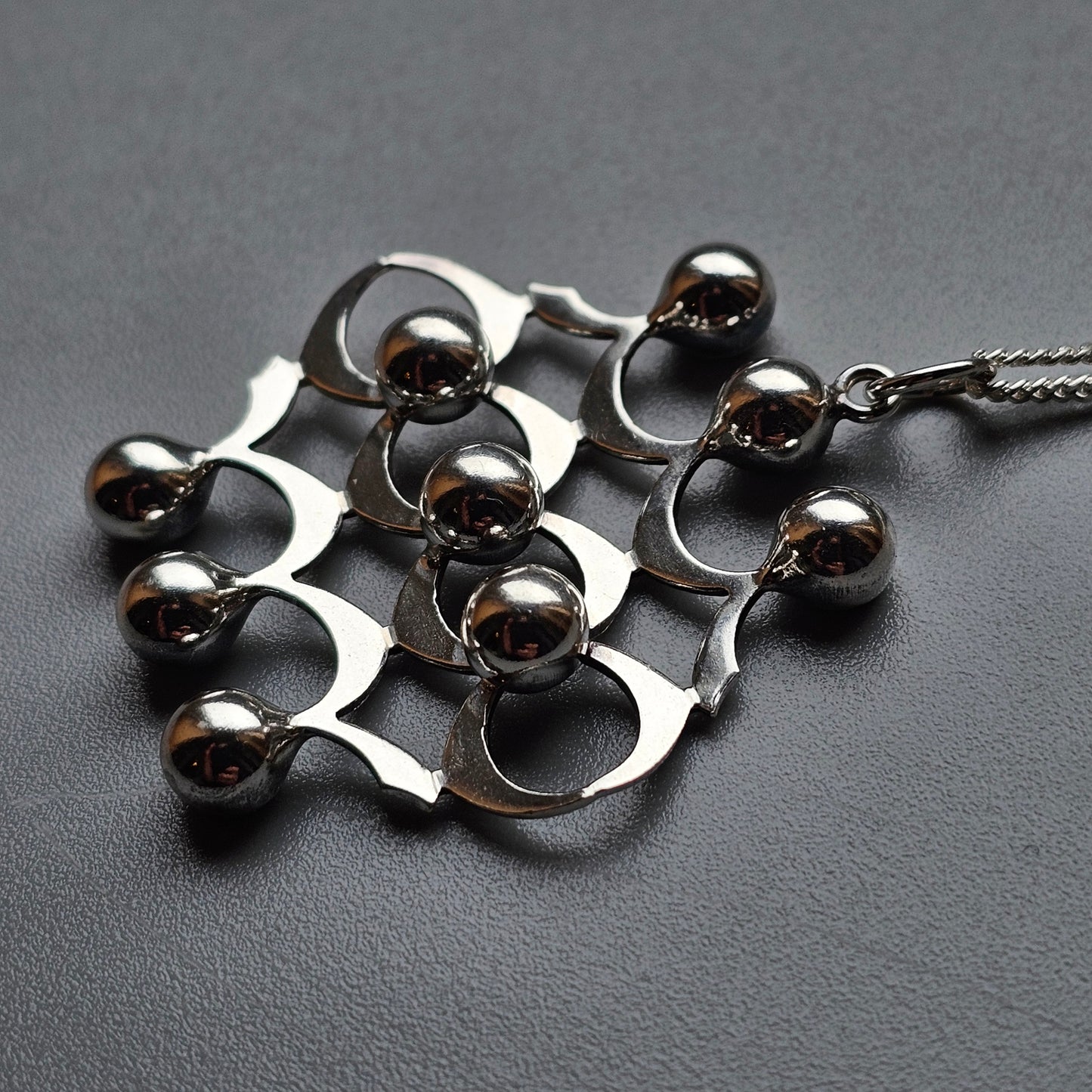 Metallic pendant featuring an abstract design with curved shapes and spherical elements.