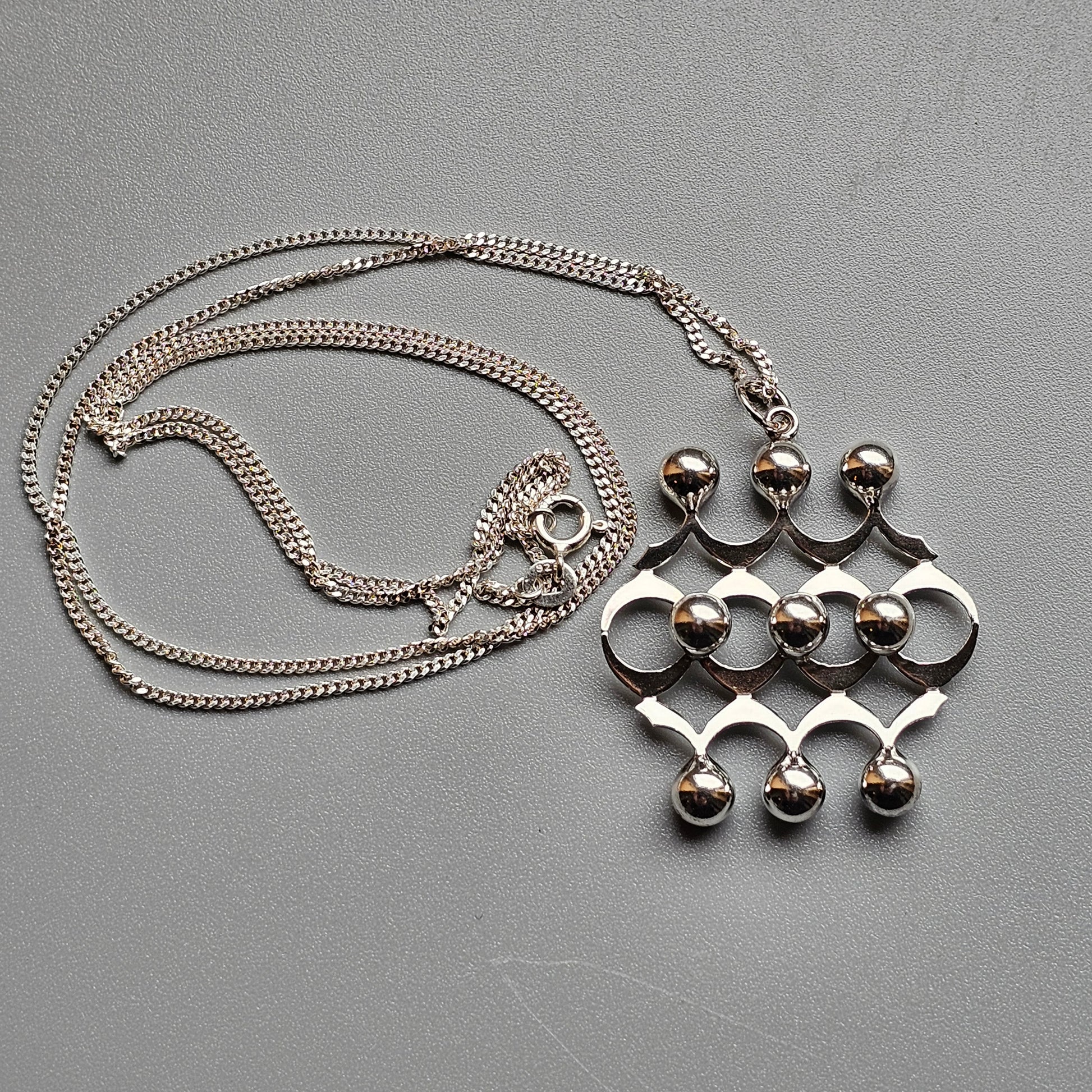 Silver pendant necklace with a geometric design featuring circles and spheres.