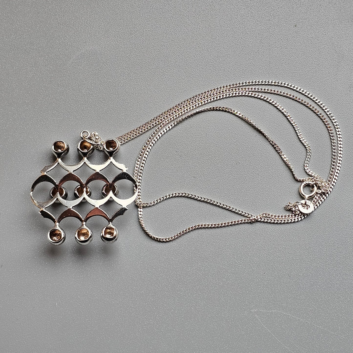 Silver pendant necklace with an abstract geometric design featuring circular elements and small gemstones.