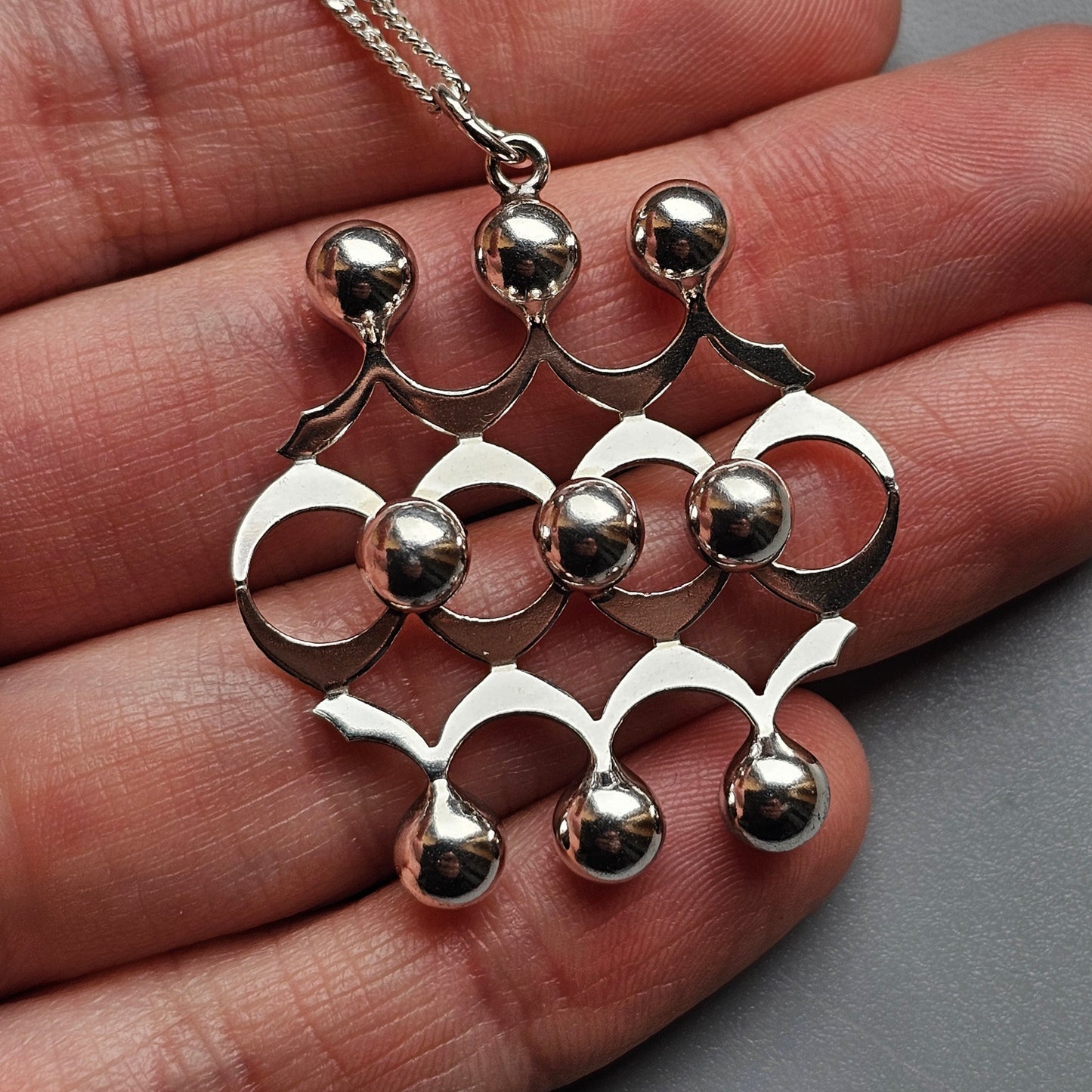 Silver pendant necklace with an abstract geometric design featuring spheres and curved shapes.