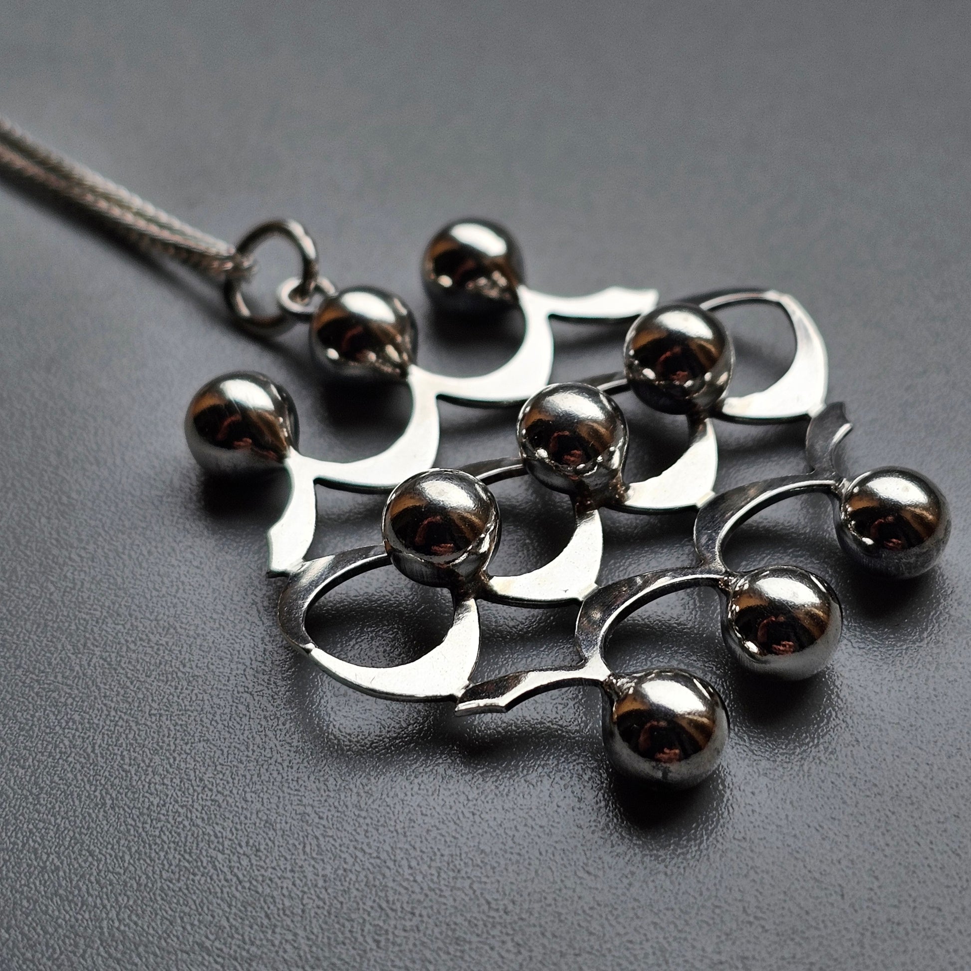 Metallic pendant necklace with curved shapes and spherical beads.