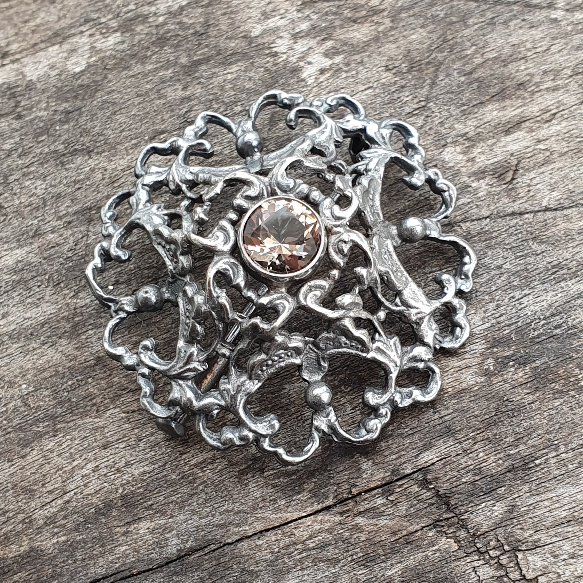 Ornate silver brooch with intricate swirling patterns and a central gemstone.