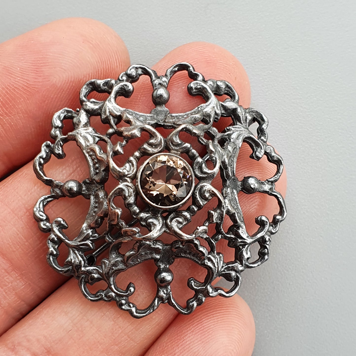 Ornate silver brooch with intricate filigree design and central gemstone.