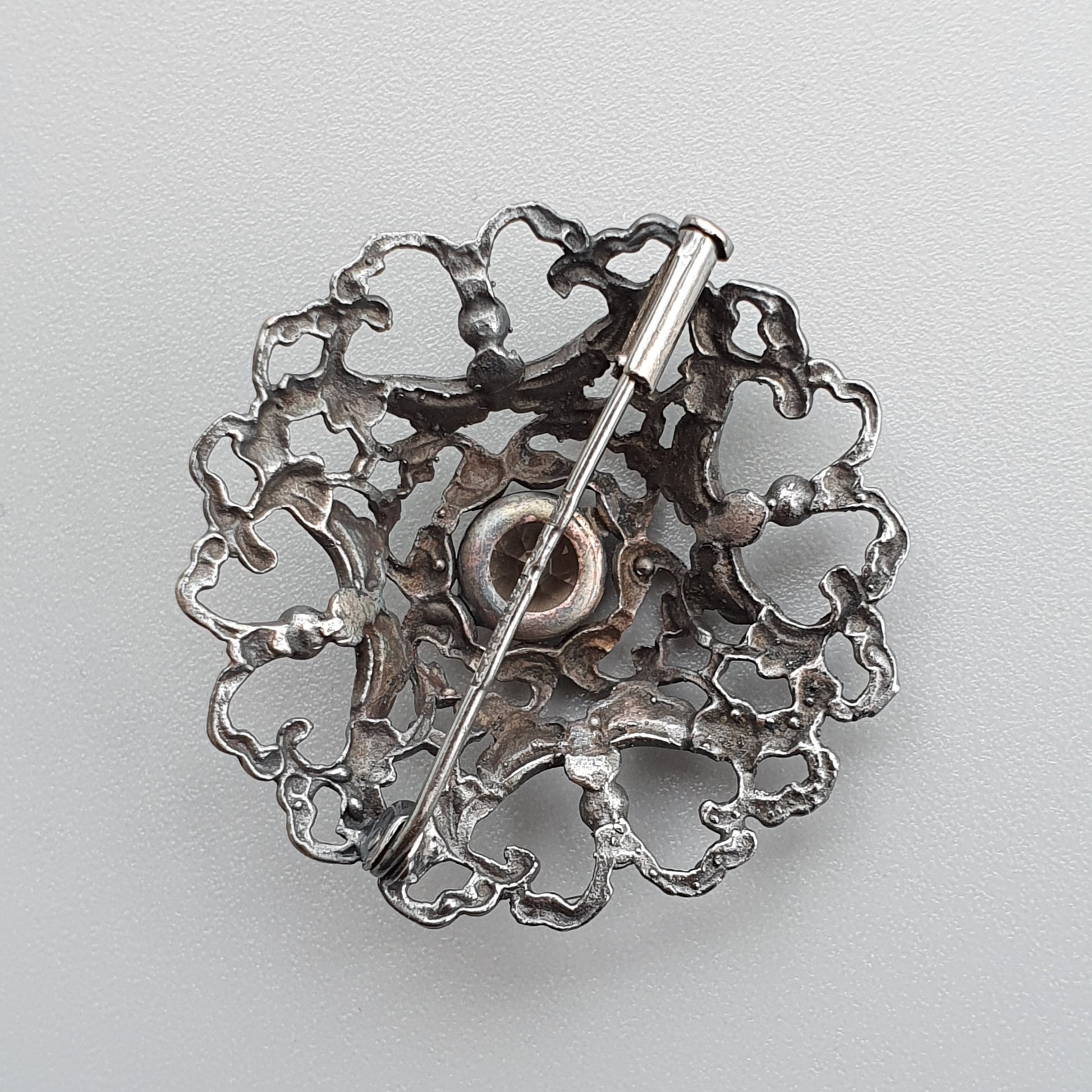 Ornate silver brooch with intricate filigree design and a central pin.