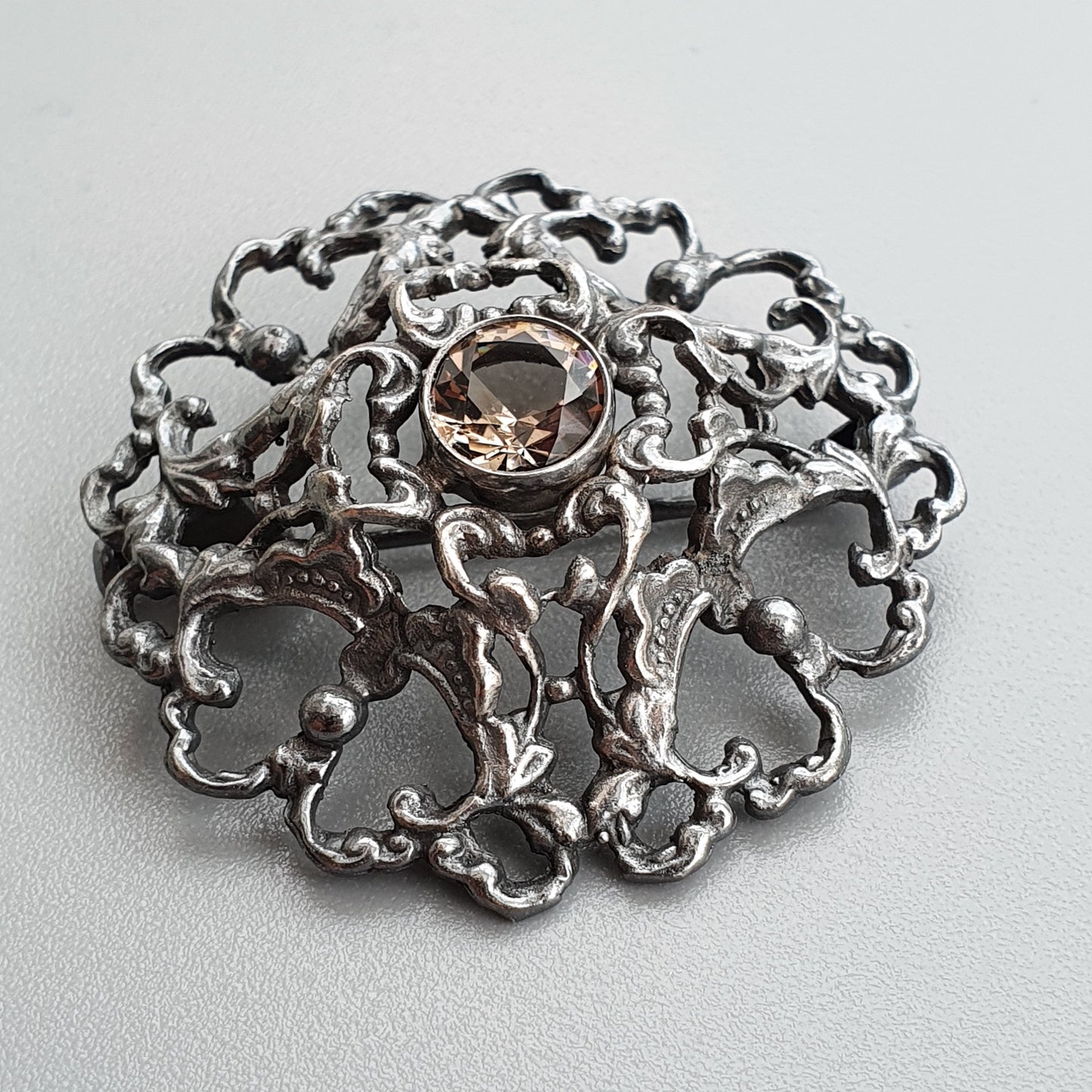 Ornate silver brooch with intricate filigree design and a central gemstone.