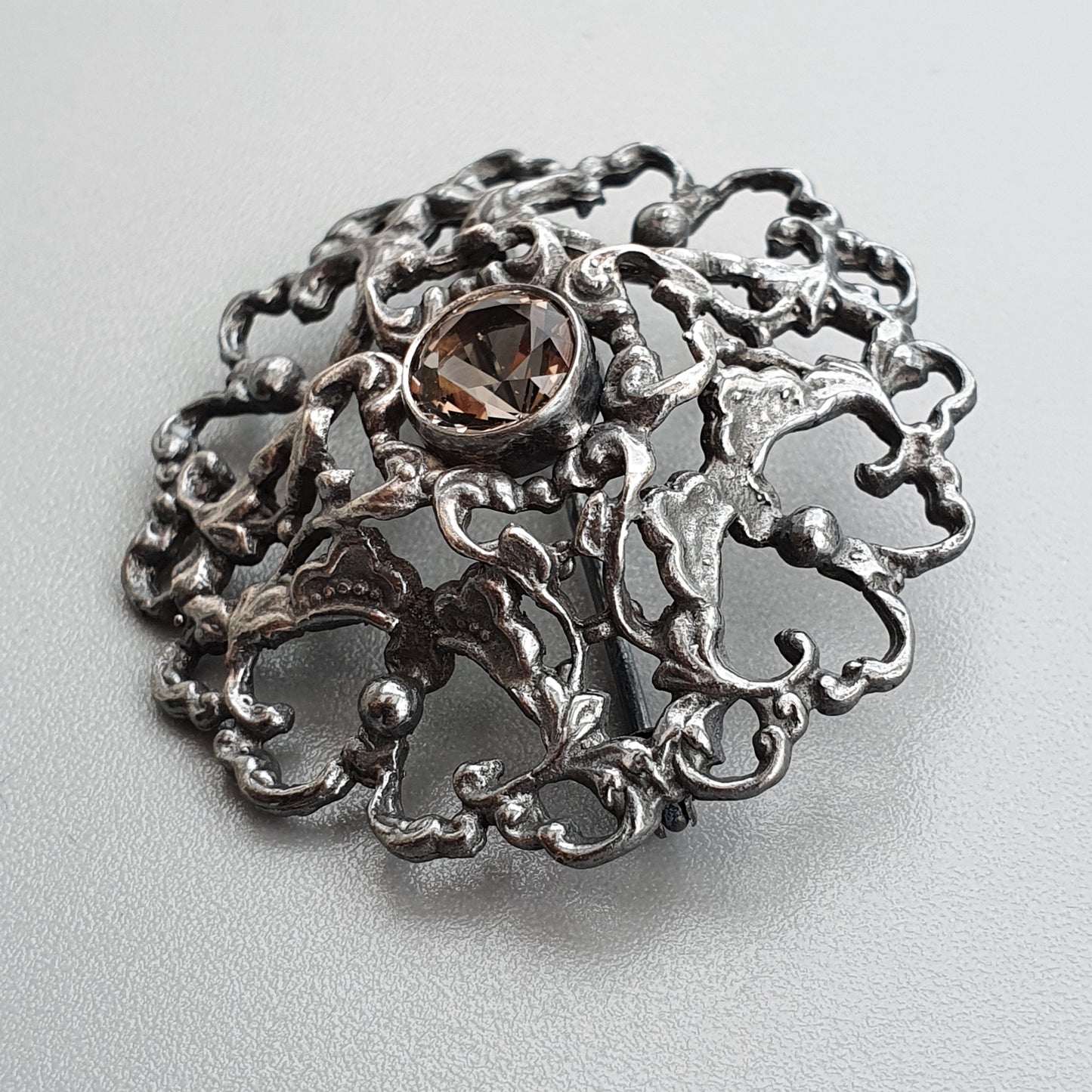 Ornate silver brooch with intricate filigree design and a central gemstone.