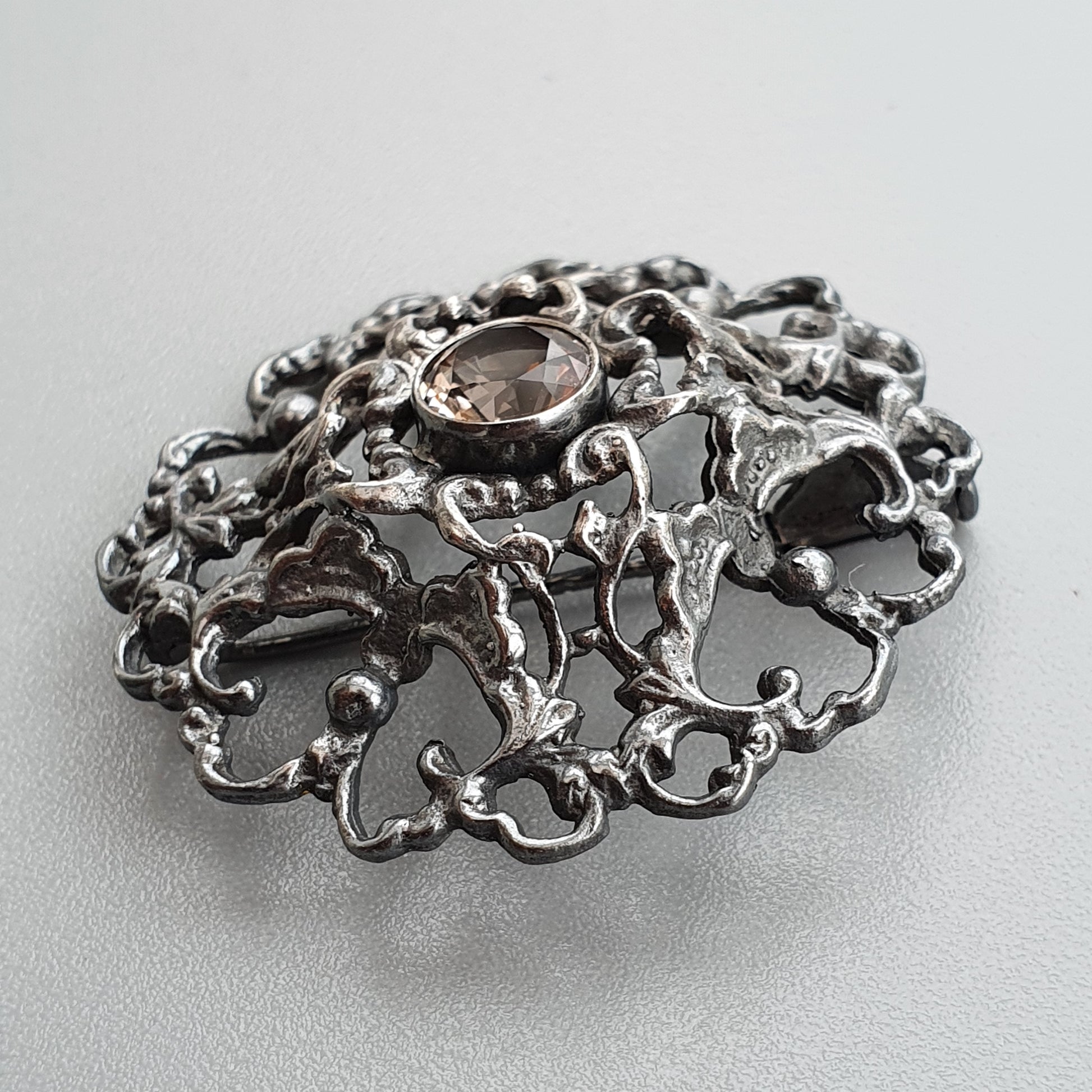 Ornate silver brooch with intricate filigree design and a central gemstone.