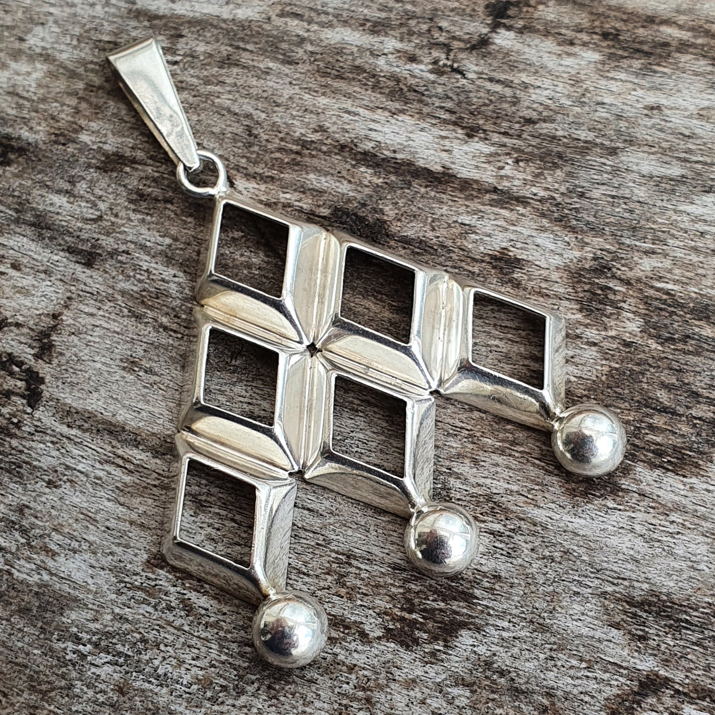 Silver pendant with a geometric design featuring squares and dangling spheres.