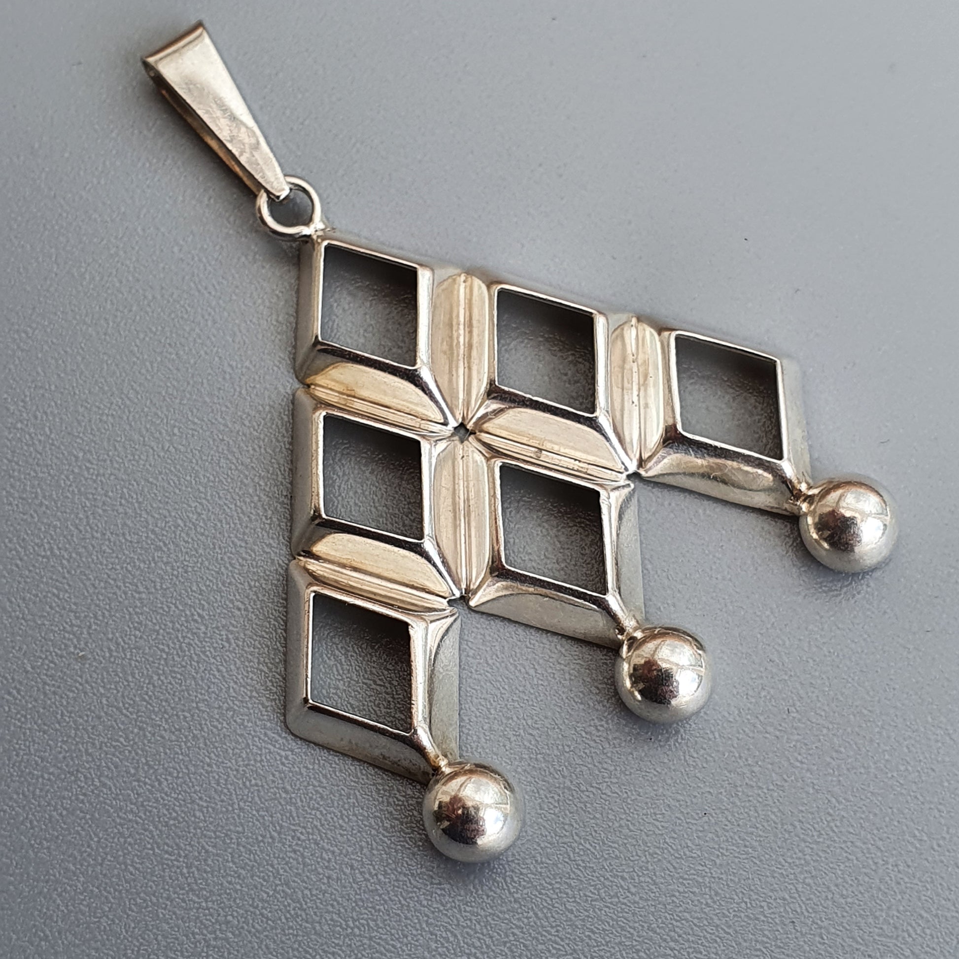 Silver pendant with a geometric design featuring diamond shapes and three small spheres.