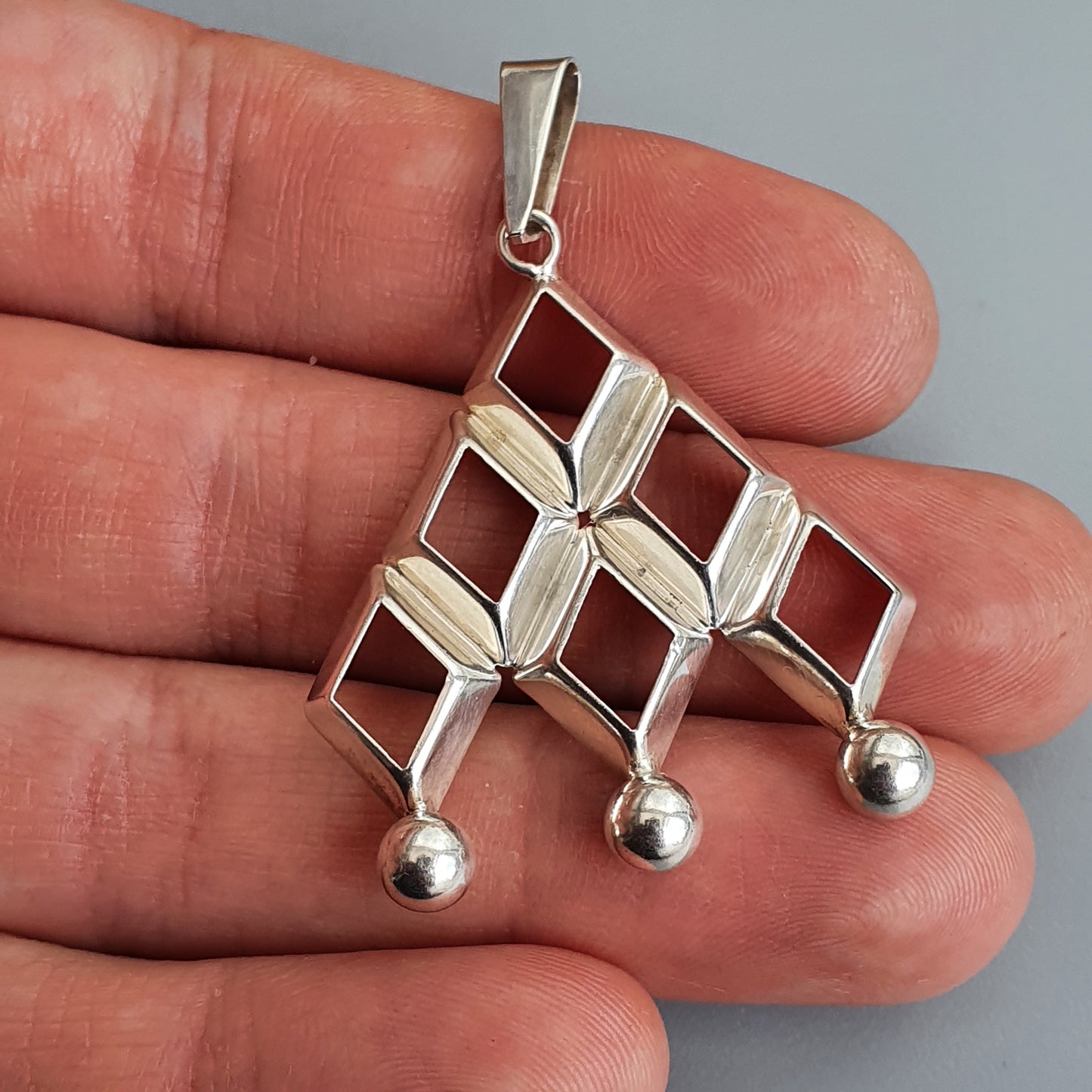 Silver pendant with a geometric design featuring diamond shapes and three small spheres at the bottom.