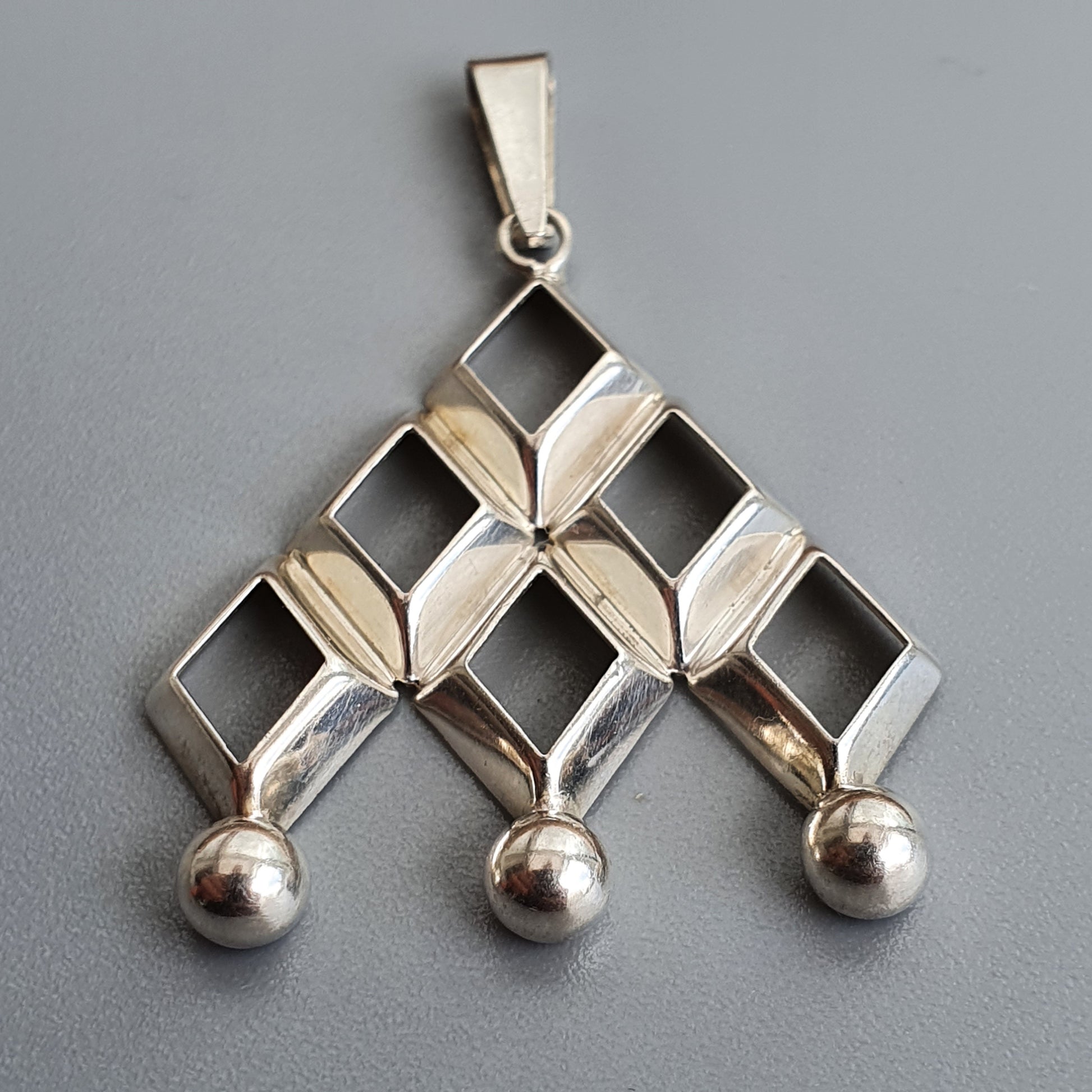 Silver pendant with a geometric design featuring squares and spheres arranged in a triangular shape.