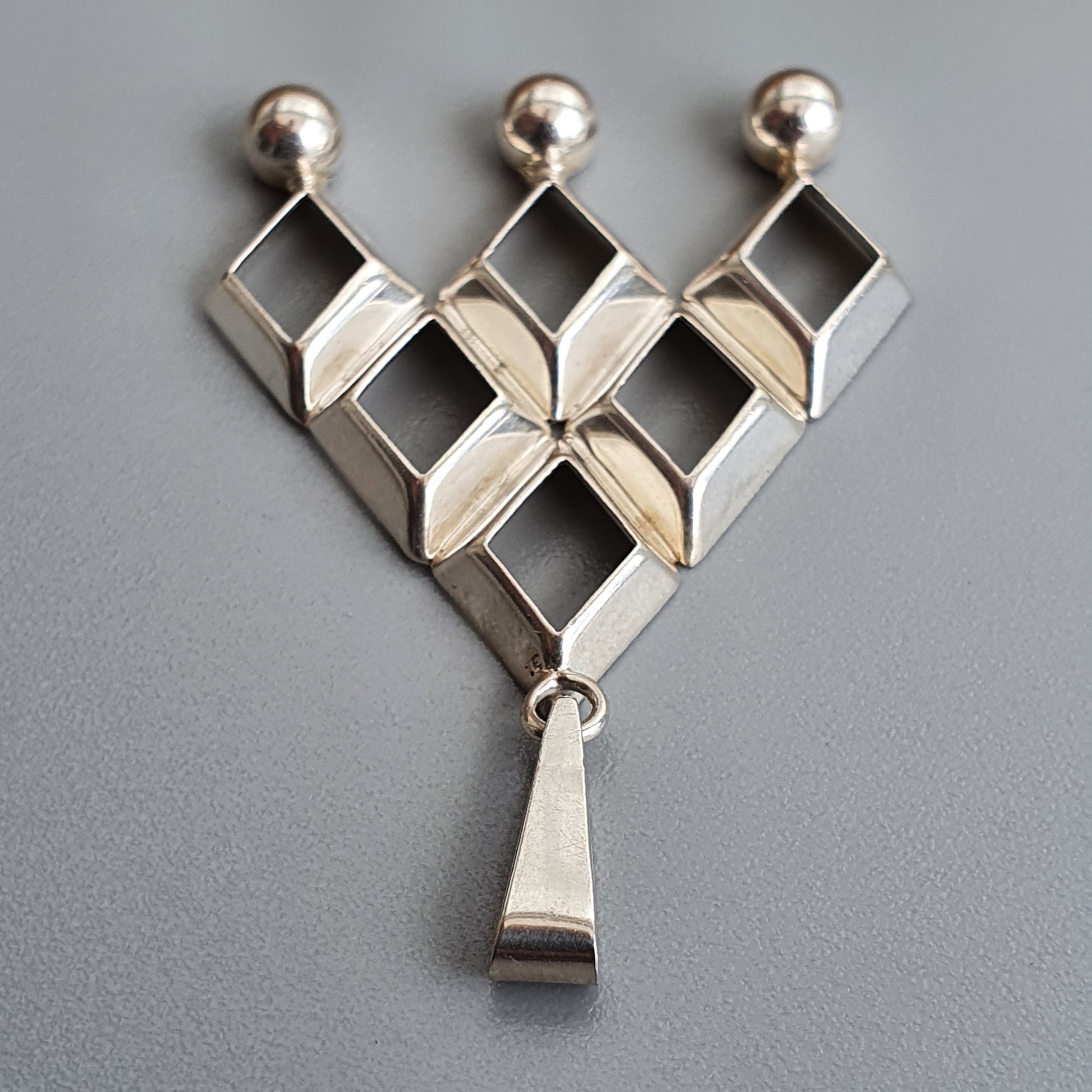 Geometric silver pendant with diamond-shaped elements and a dangling triangular piece.