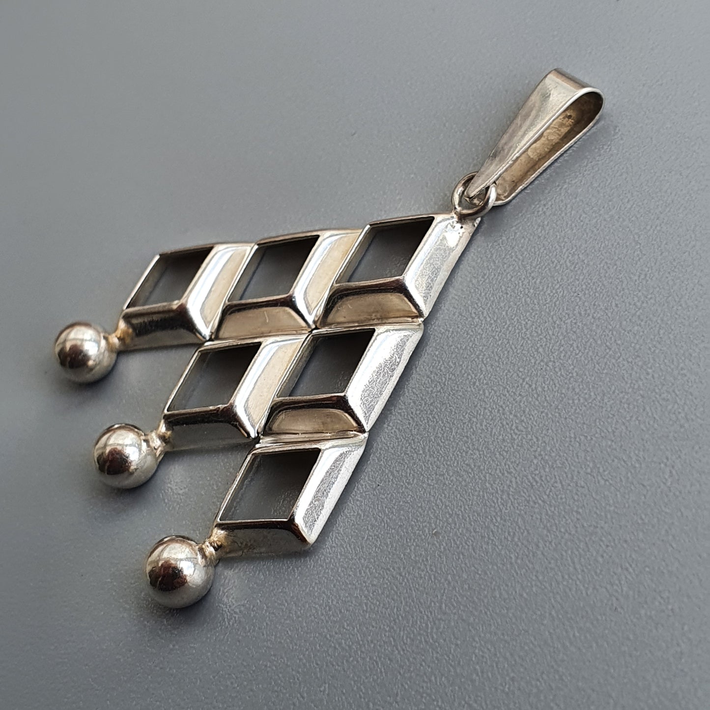 Silver pendant with a geometric design featuring rectangular shapes and three small spheres.