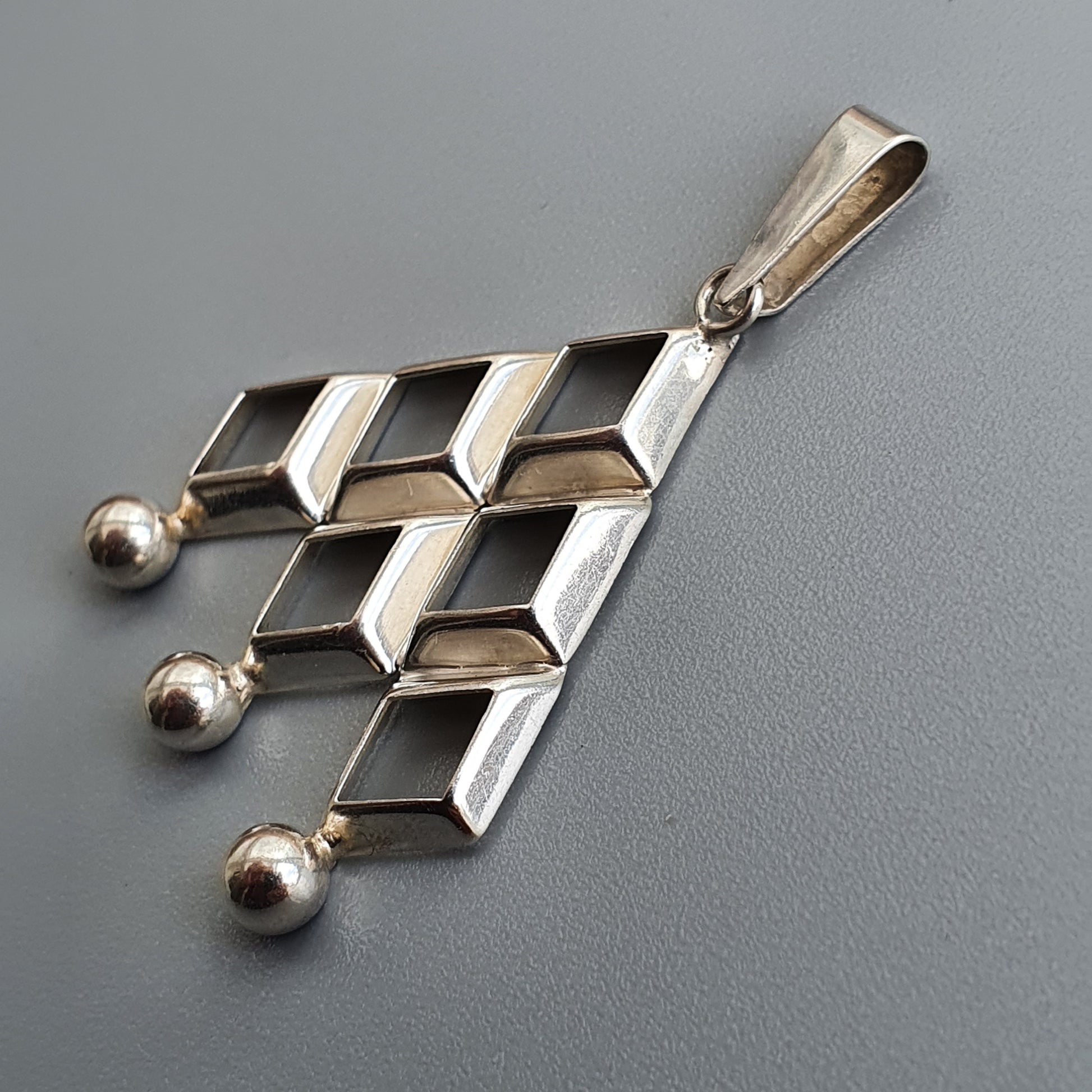 Silver pendant with a geometric design featuring rectangular shapes and three small spheres.