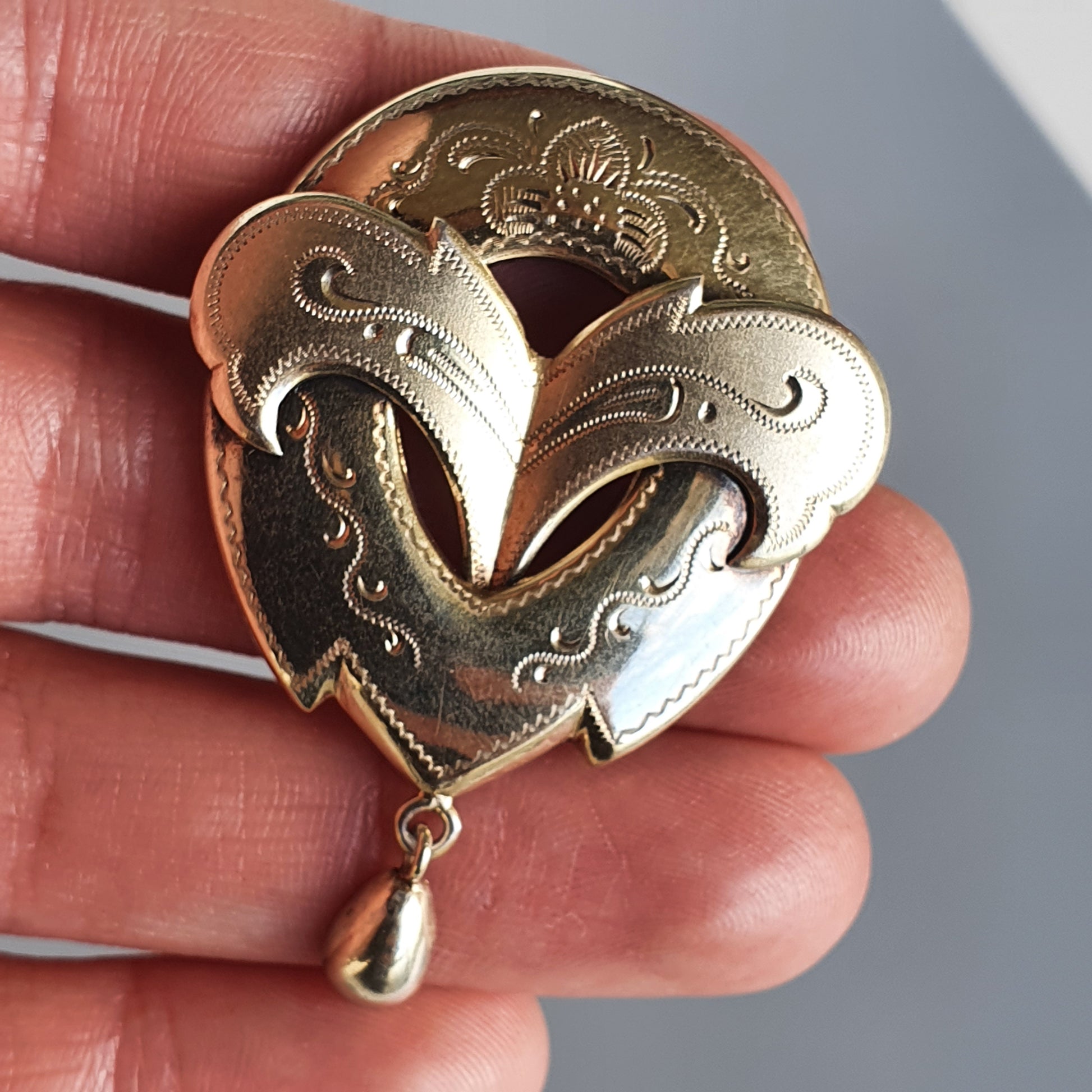 Ornate heart-shaped brooch with intricate engravings and a dangling teardrop pendant.