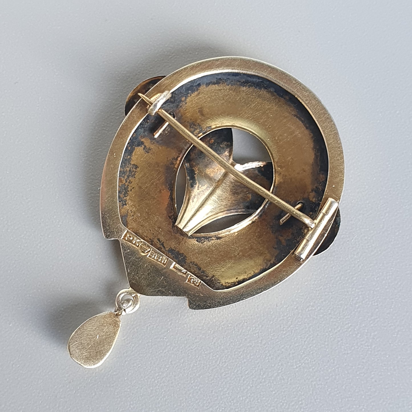 Antique brass or gold-toned sundial-like brooch with geometric design and a dangling teardrop pendant.