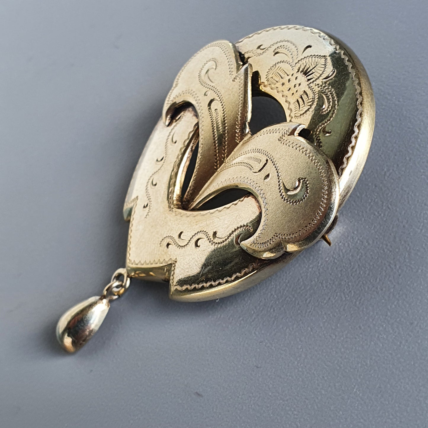 Ornate gold brooch with floral and swirling designs featuring a teardrop-shaped pendant.