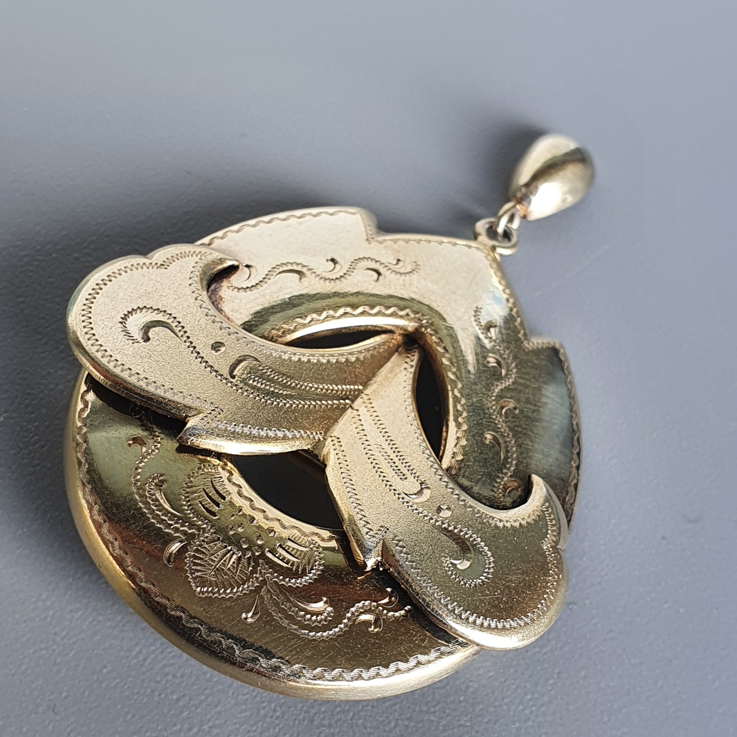 Ornate gold pendant with intricate swirling designs resembling a stylized bird or phoenix.