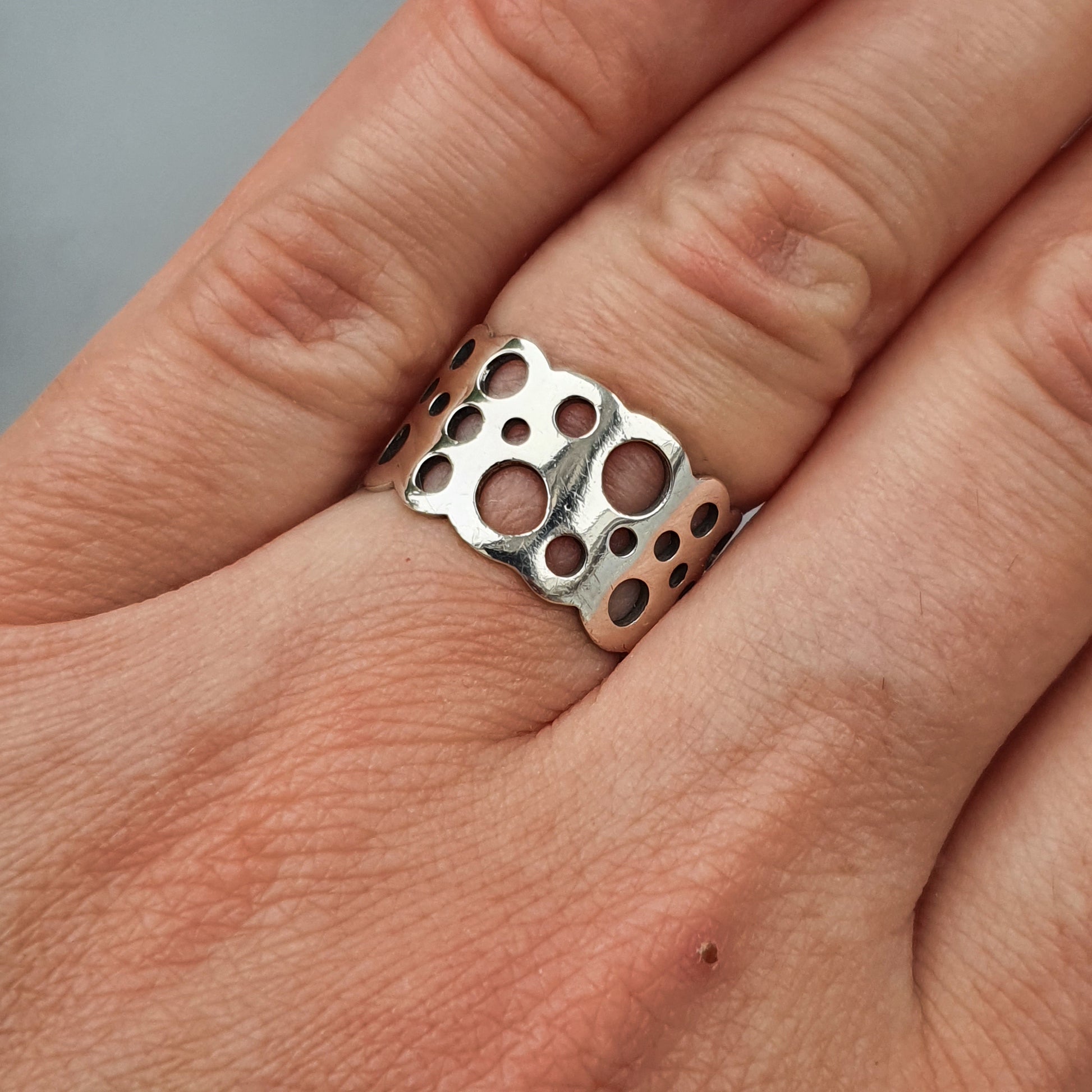 Silver ring with circular cutout patterns worn on a finger.