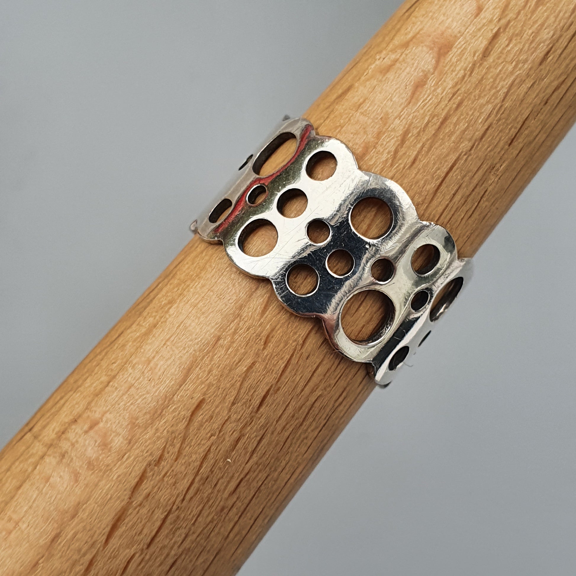 Metal ring with circular cutouts wrapped around a wooden dowel.