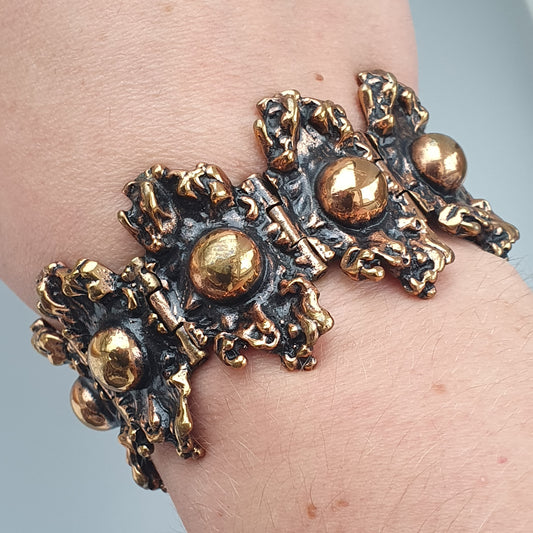 Ornate metallic bracelet with intricate designs and gold-colored spherical accents.