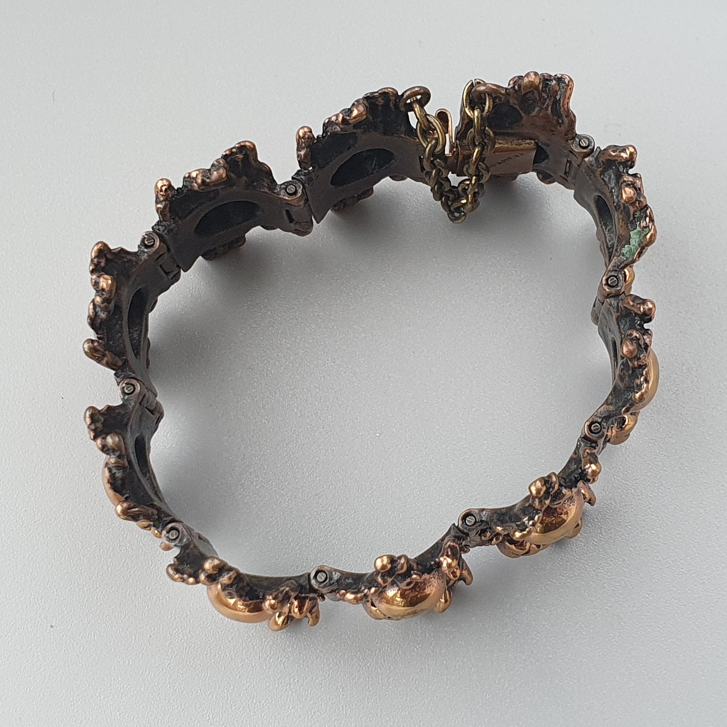 Irregularly shaped metallic bracelet with a rough, textured surface and organic-looking edges.