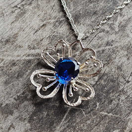 Silver flower-shaped pendant necklace with a blue gemstone center.