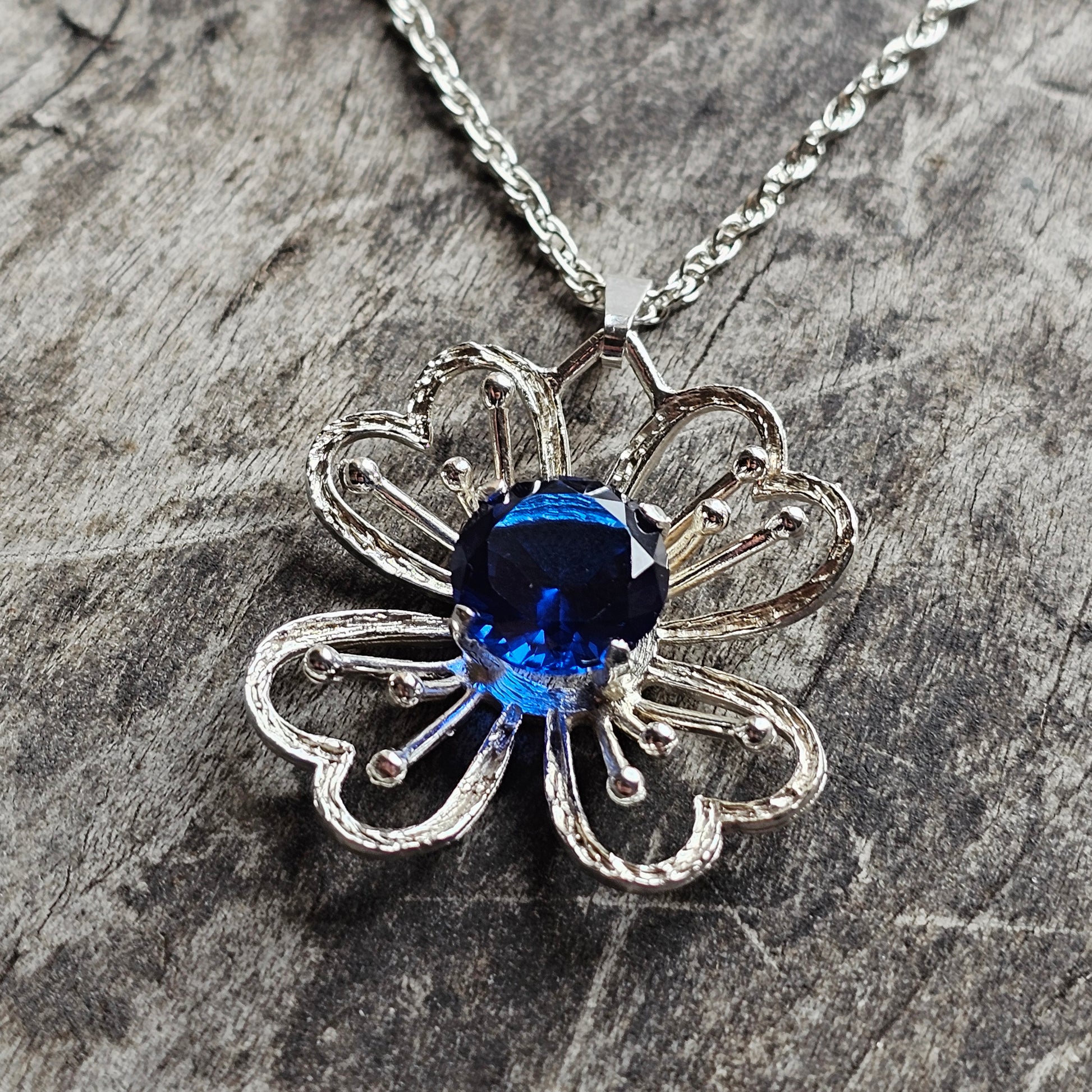 Silver flower-shaped pendant necklace with a blue gemstone center.