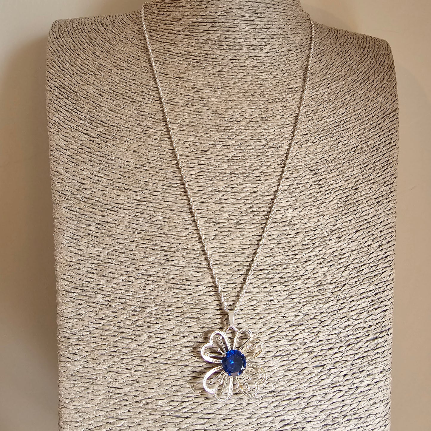 Silver flower-shaped pendant necklace with a blue gemstone center.