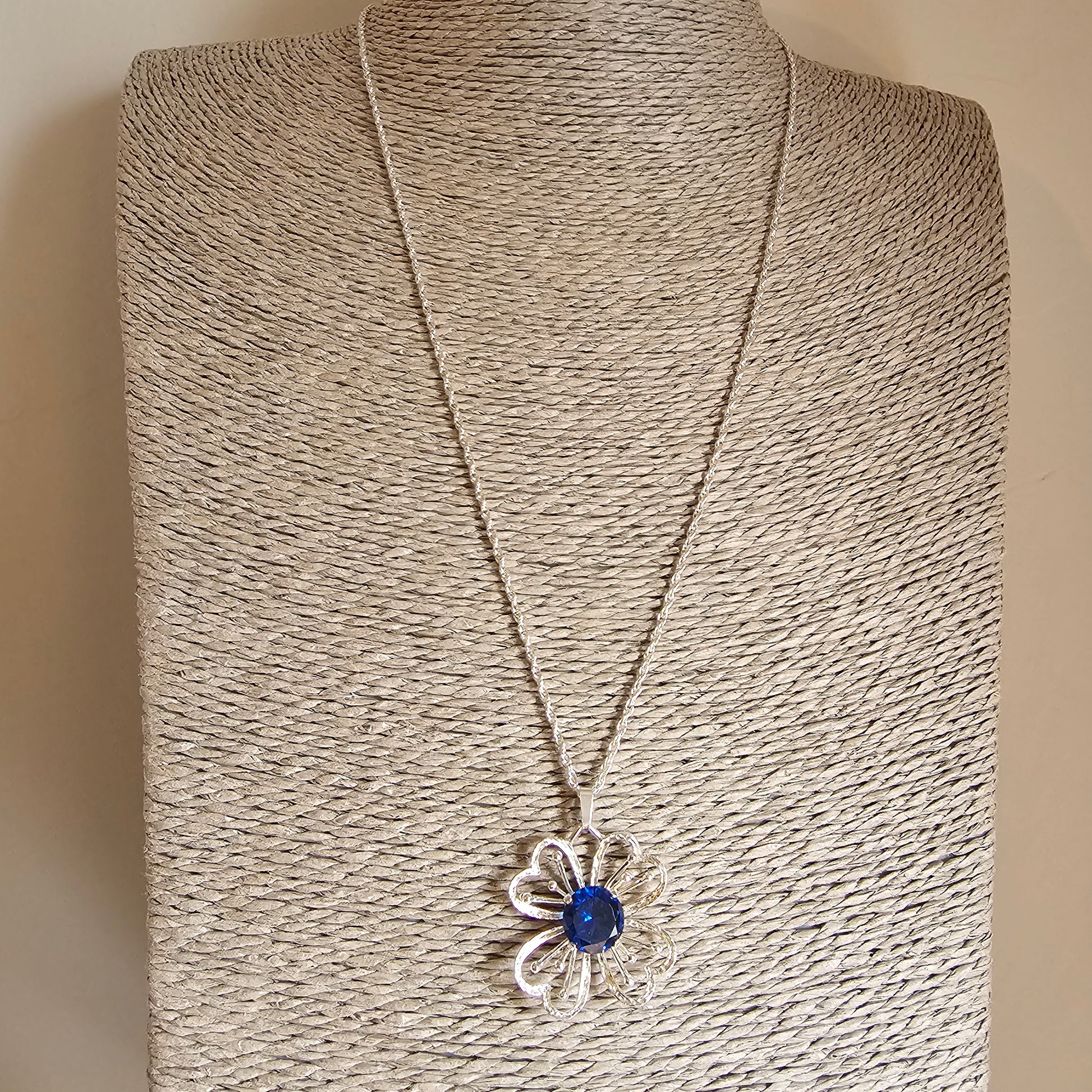 Silver flower-shaped pendant necklace with a blue gemstone center.