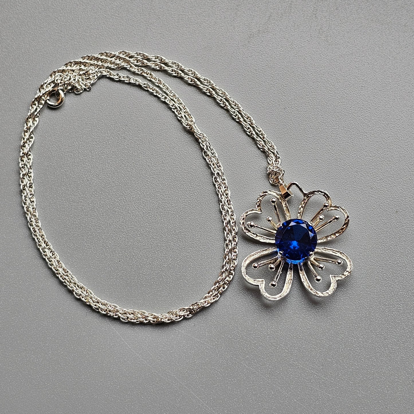 Silver necklace with a flower-shaped pendant featuring a blue gemstone center.