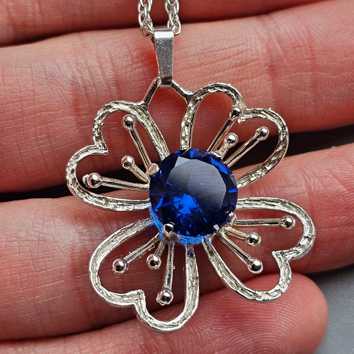 Silver flower-shaped pendant necklace with a blue gemstone center.