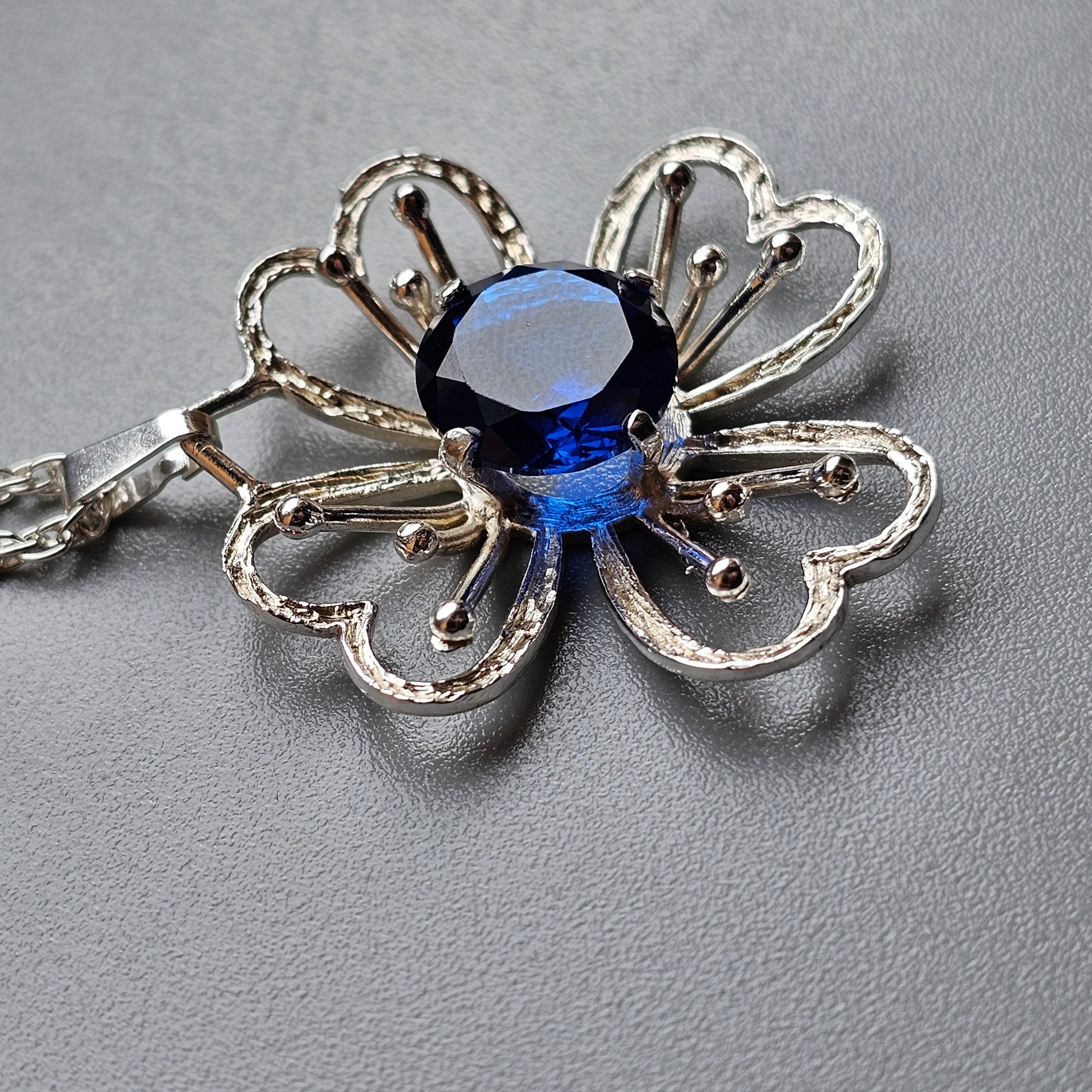 Silver flower-shaped brooch with a central blue gemstone.