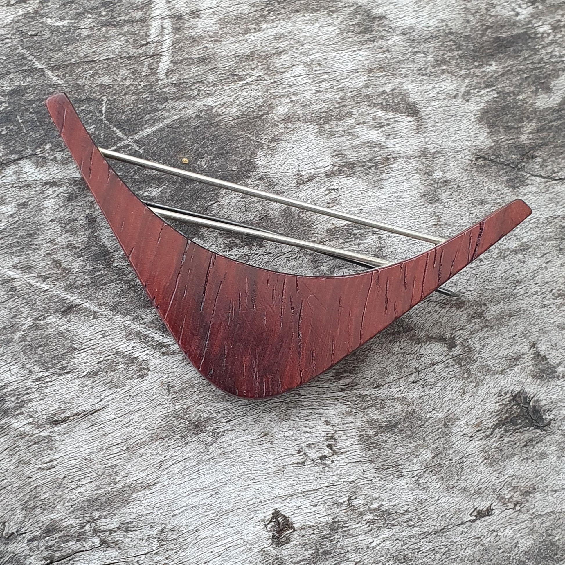 Curved red wooden object with two metal rods attached.