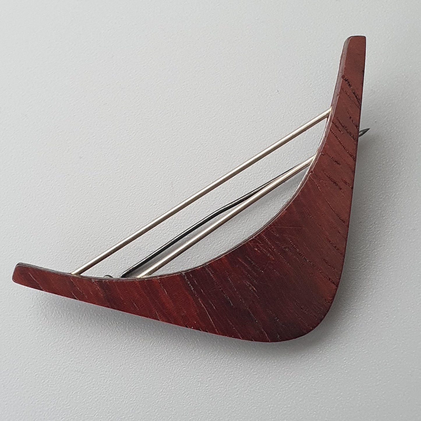 Curved red wooden object with three metal strings resembling a musical instrument.