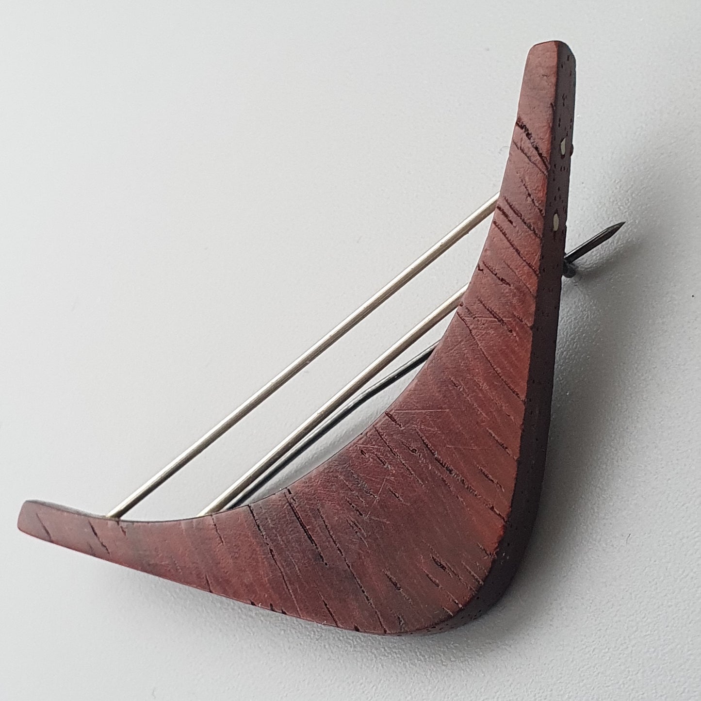 Curved wooden object resembling a boomerang with metal prongs attached.