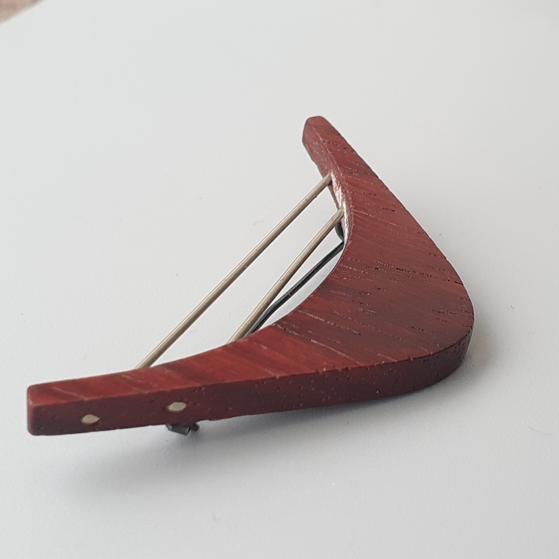 Red wooden boomerang with metal pins or rods attached.