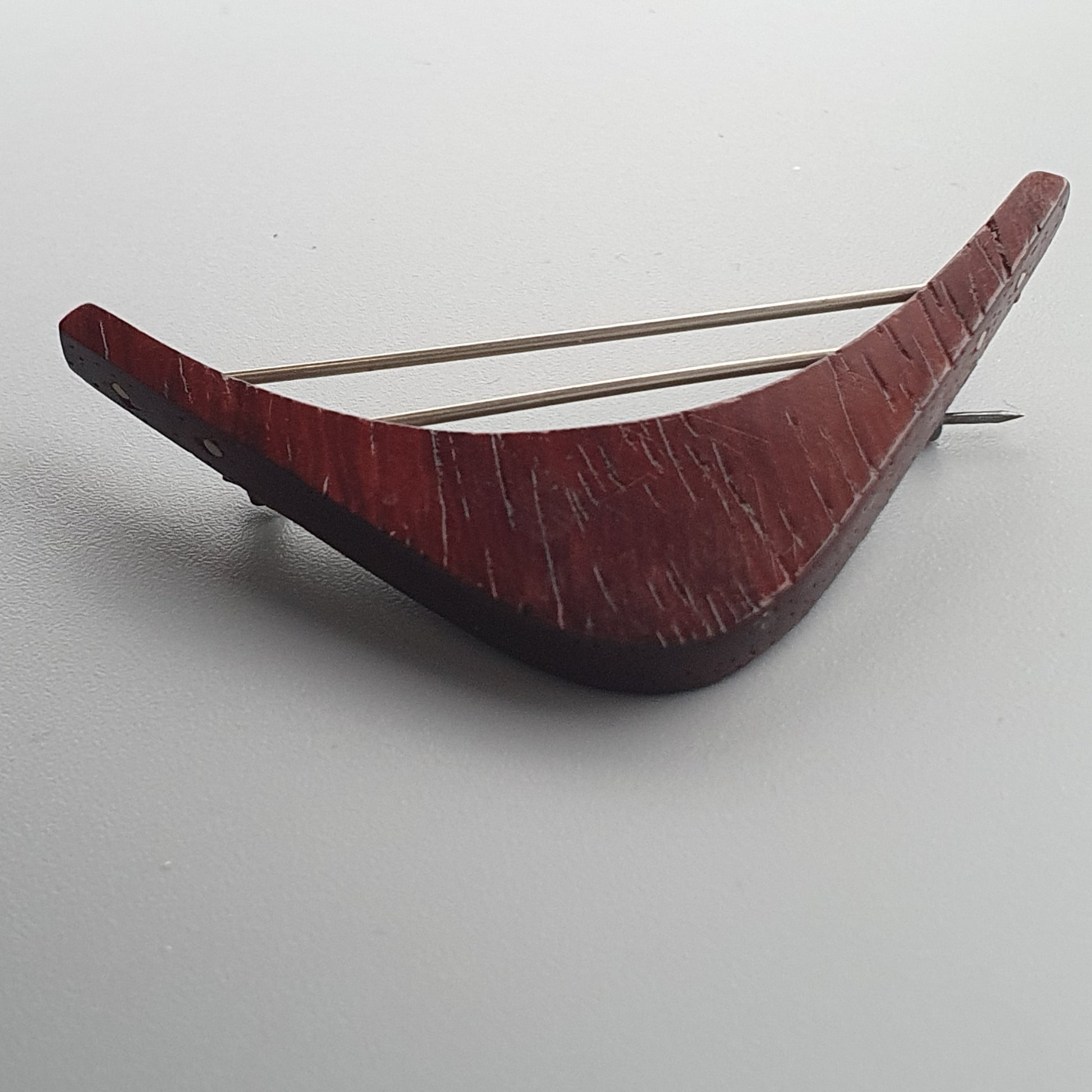 Curved red wooden object with two metal strings, resembling a simple stringed instrument.