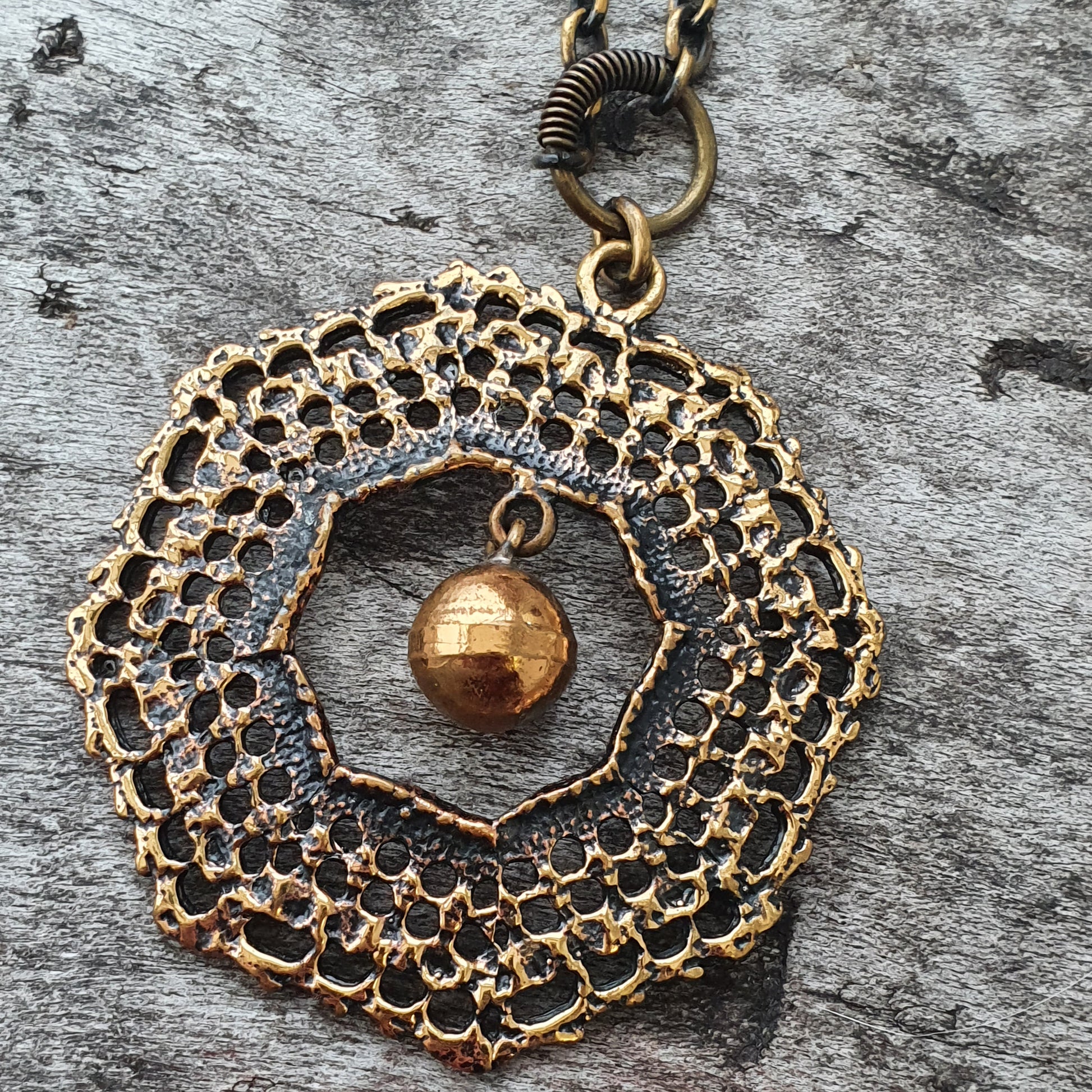 Intricate gold-toned pendant with a circular lace-like pattern and a small sphere hanging in the center.