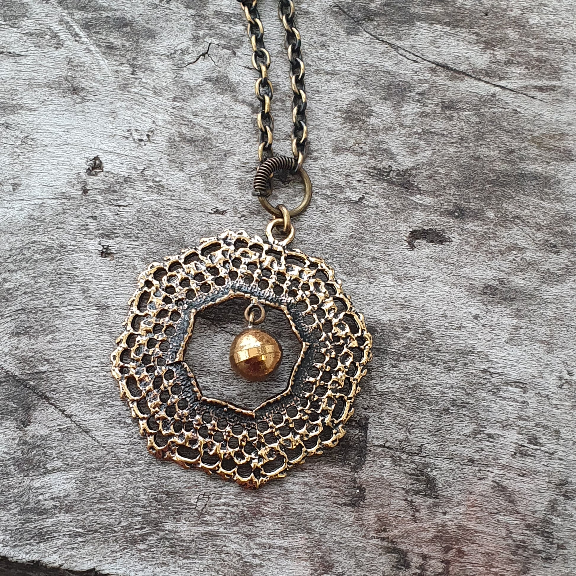 Intricate gold-toned pendant necklace with a circular filigree design and a small dangling bead at its center.