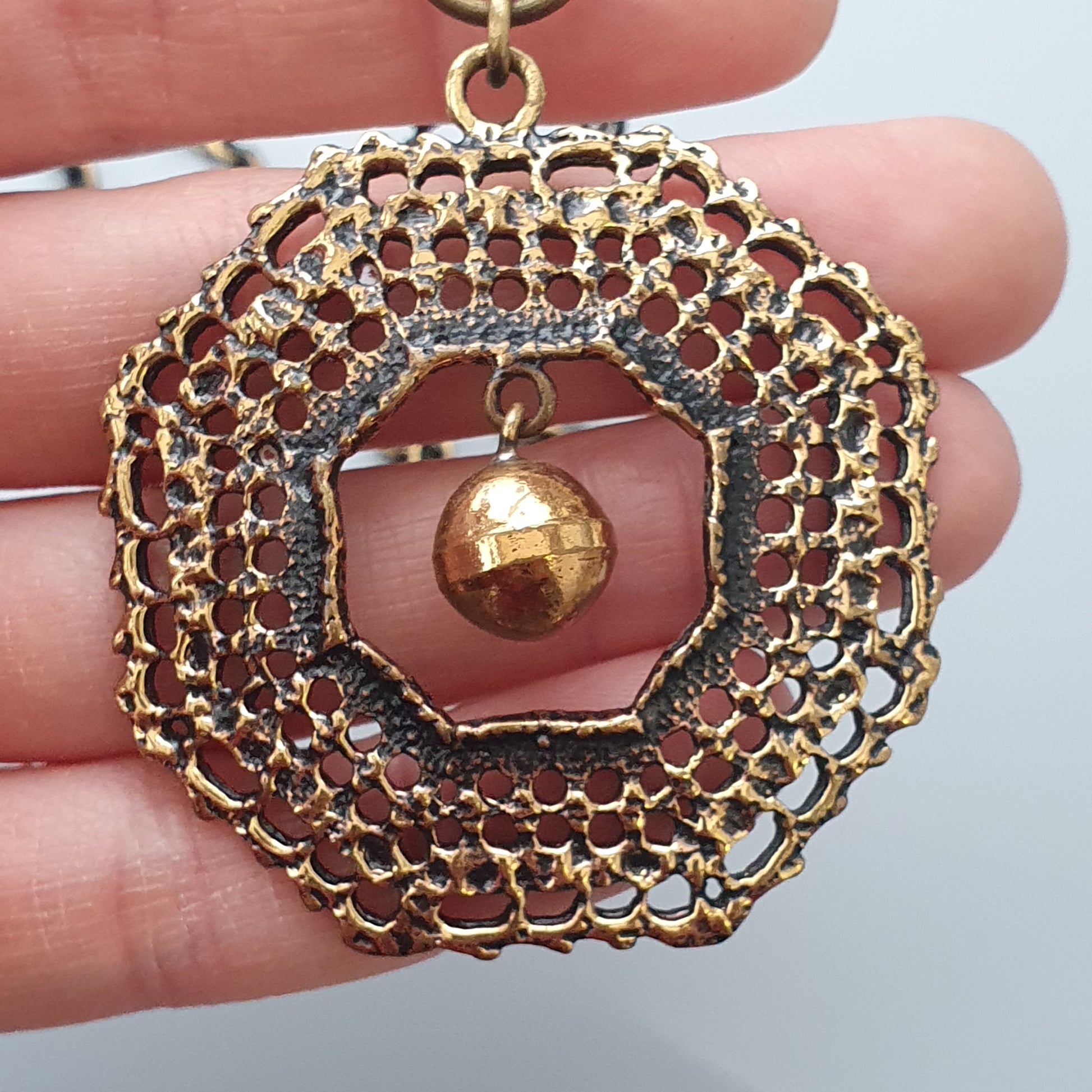 Ornate gold-toned pendant with intricate filigree design and a central hanging bead.