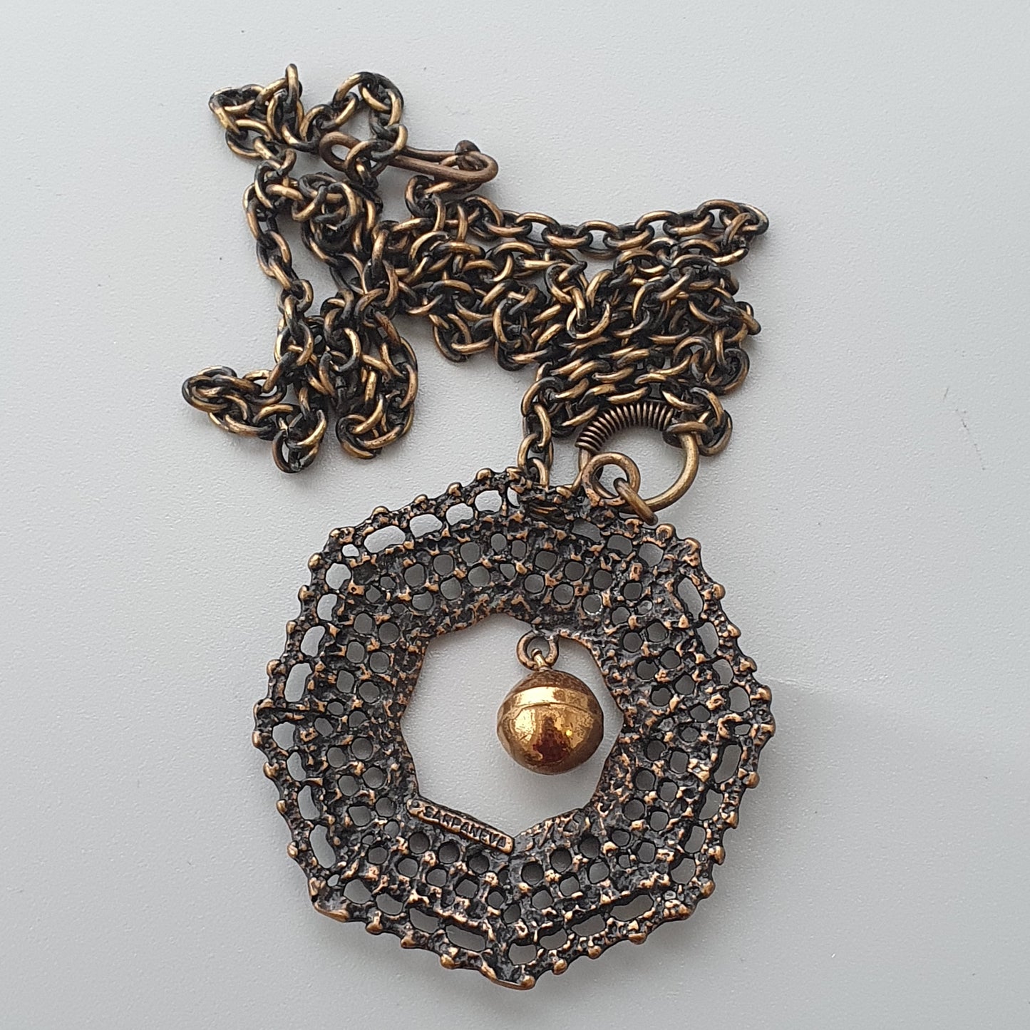 Ornate circular pendant with intricate metalwork and a small gold bead at its center, hanging from a chain.