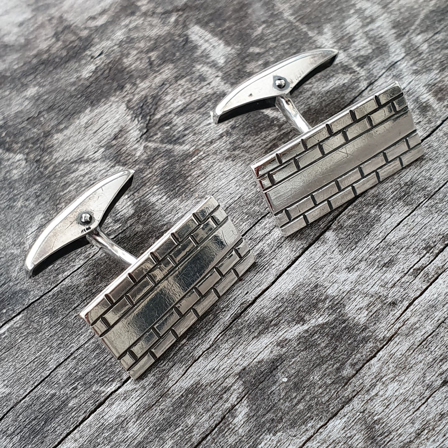 Pair of silver cufflinks with a geometric brick-like pattern design.